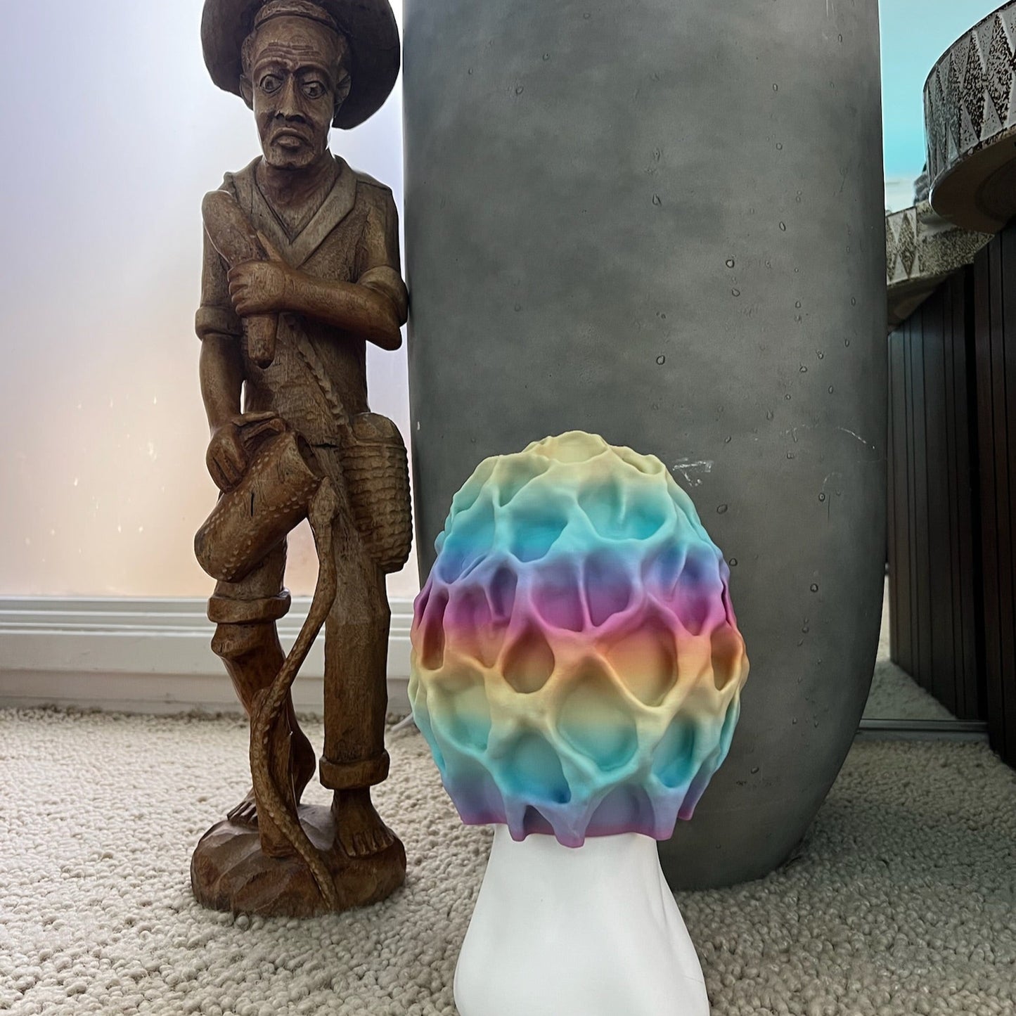Colorful Morel-inspired illuminated table lamp next to a decorative wooden figure and potted plant.