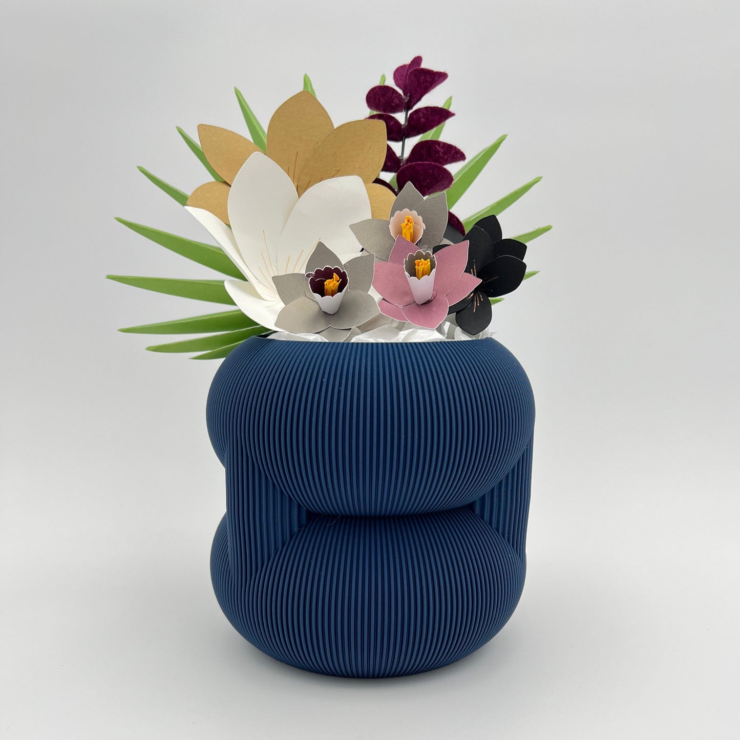 A trendy blue rounded stacked planter adorned with colorful paper flowers, perfect for a unique home decor piece.