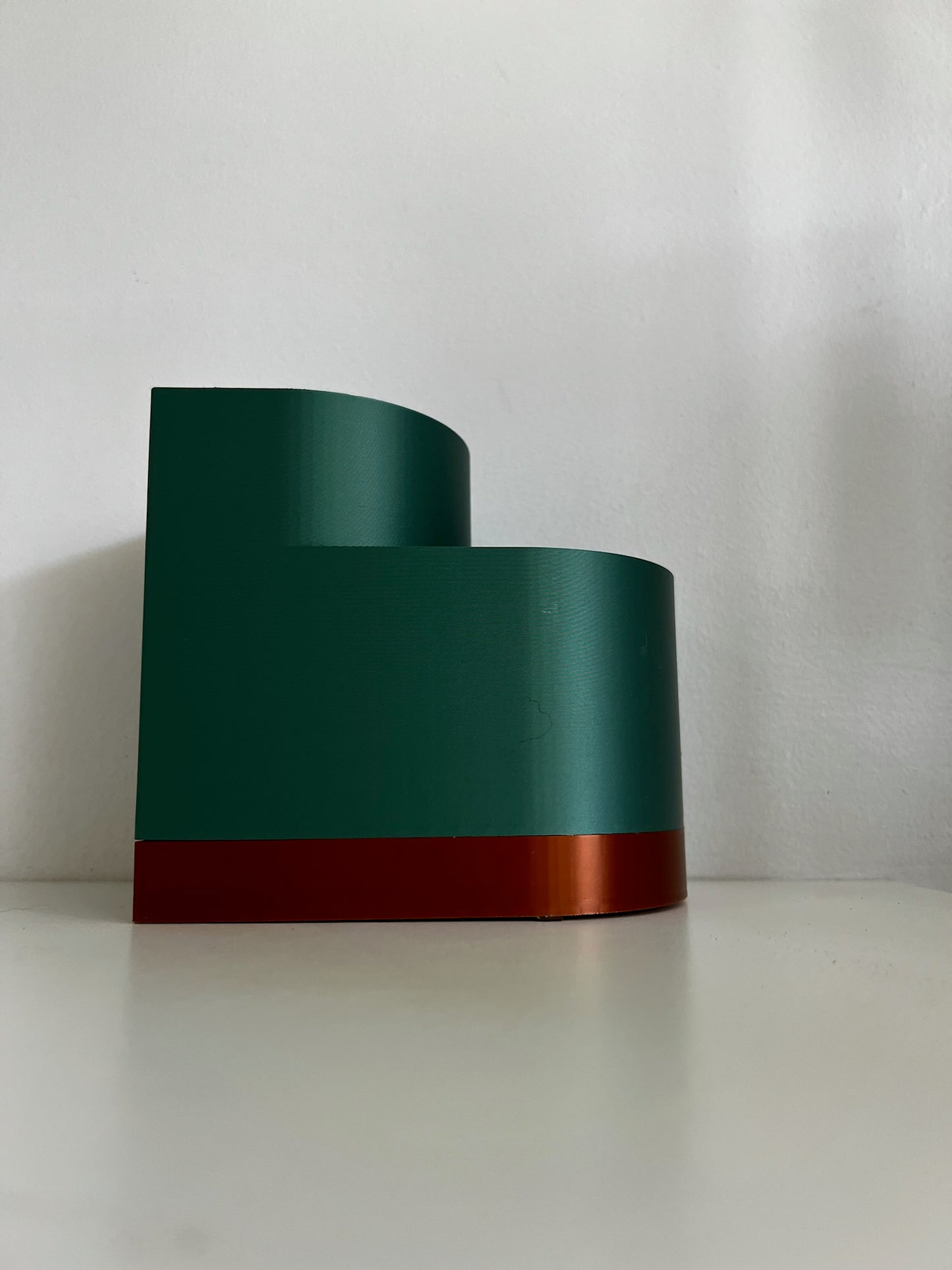 Side view of a dark green double layer planter, highlighting its sleek design and contrasting orange base.
