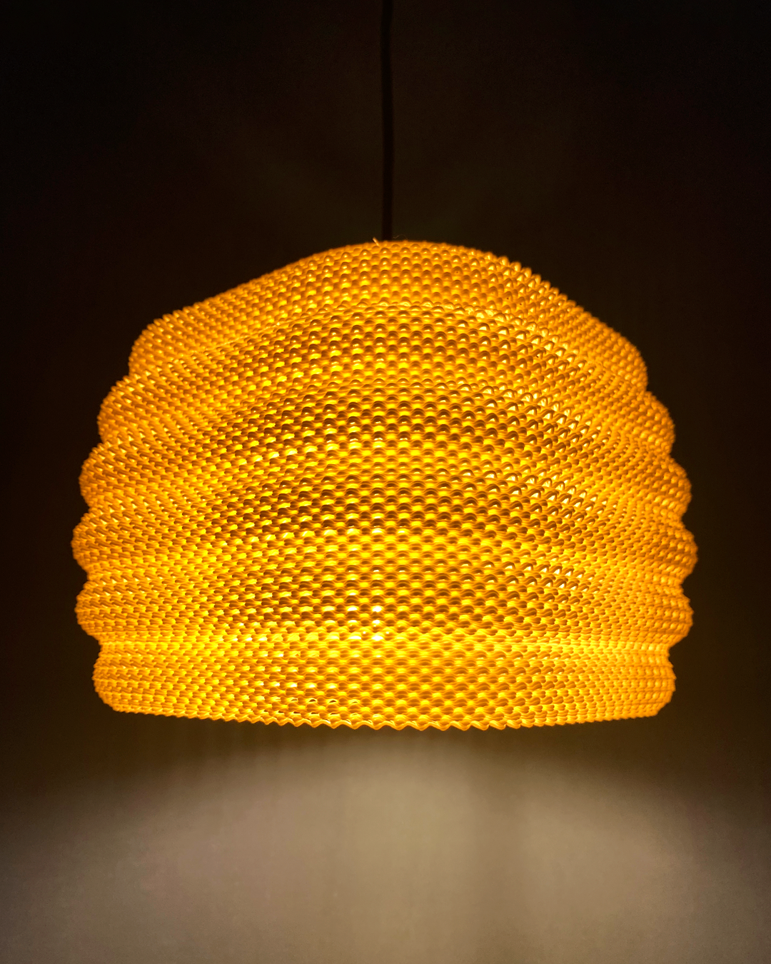 Daira Lampshade glowing in orange against a dark background, emphasizing its unique woven texture and charming light diffusion.