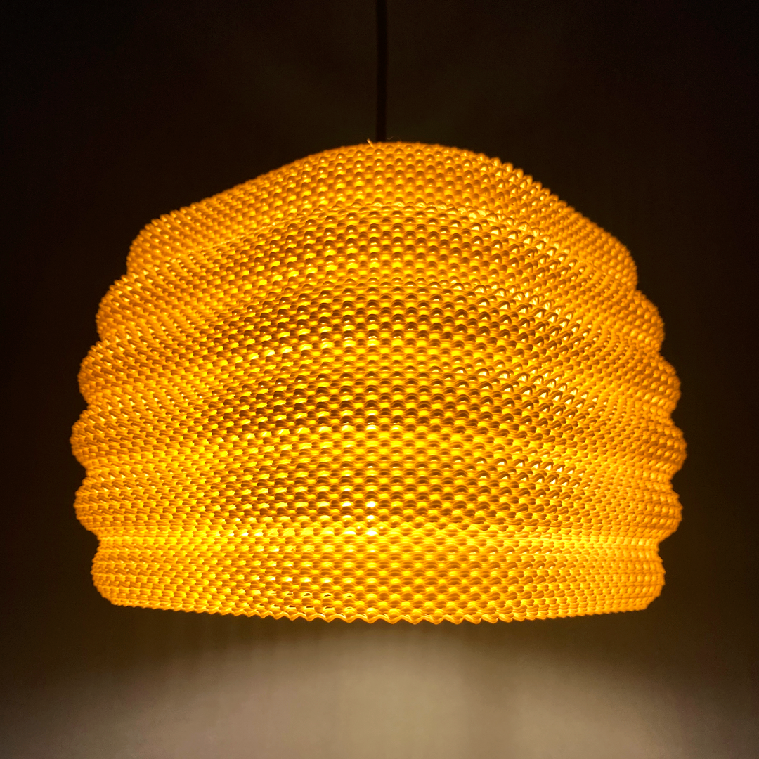 Daira Lampshade glowing in orange against a dark background, emphasizing its unique woven texture and charming light diffusion.