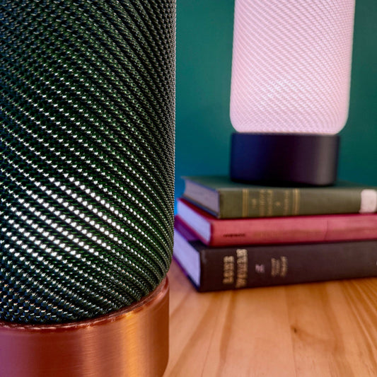 Close-up view of stylish EVE Table Lamps featuring textured cylindrical shades in green and white. These modern minimalist lamps illuminate books resting on a wooden table.