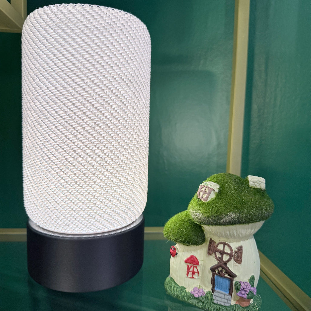Elegant white EVE Table Lamp with a textured cylindrical shade displayed alongside a whimsical mushroom-shaped decoration against a vibrant green background.