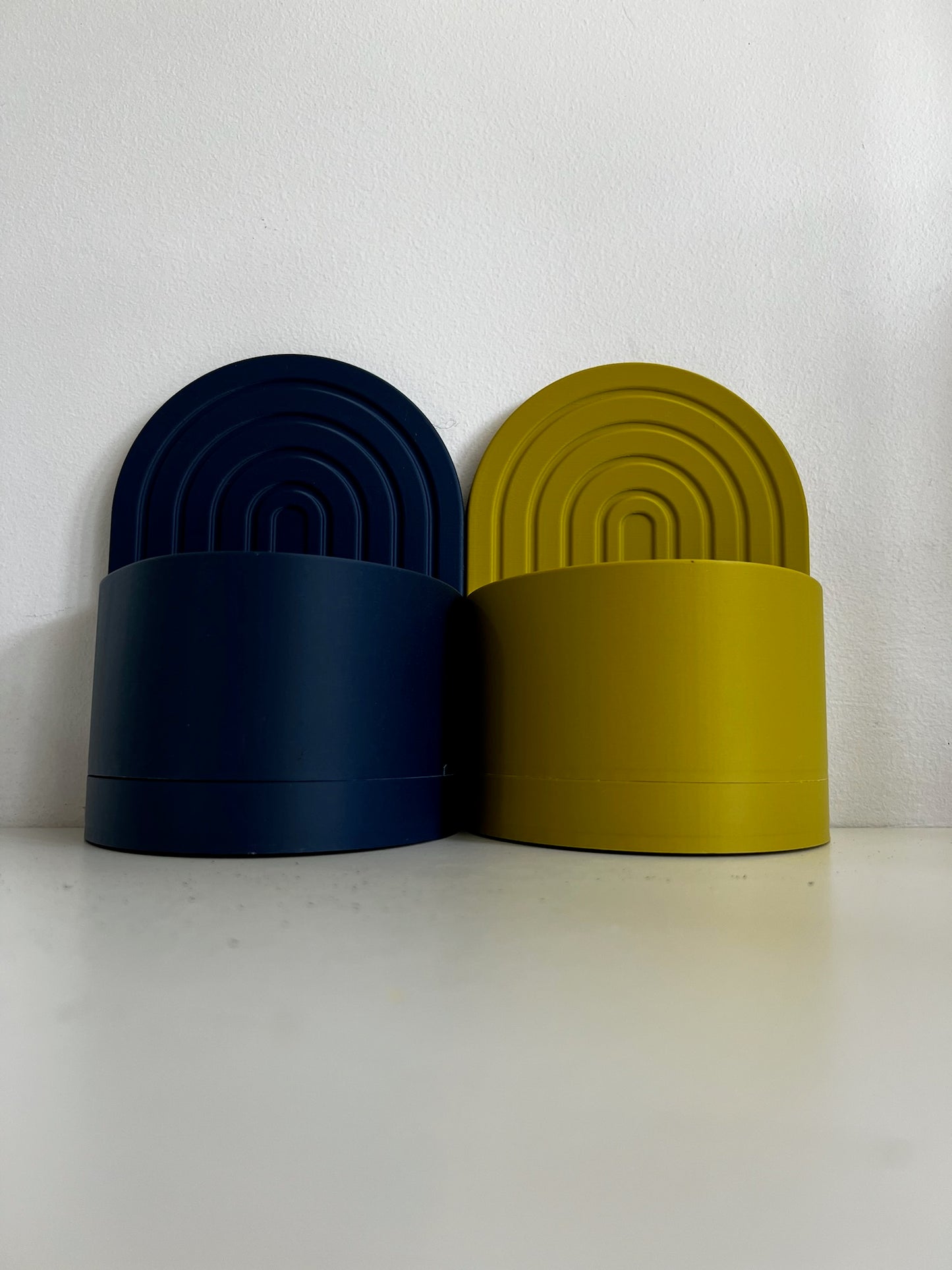 Two stylish arch bookend planters, one navy blue and one yellow, side by side against a white wall for a contemporary look.