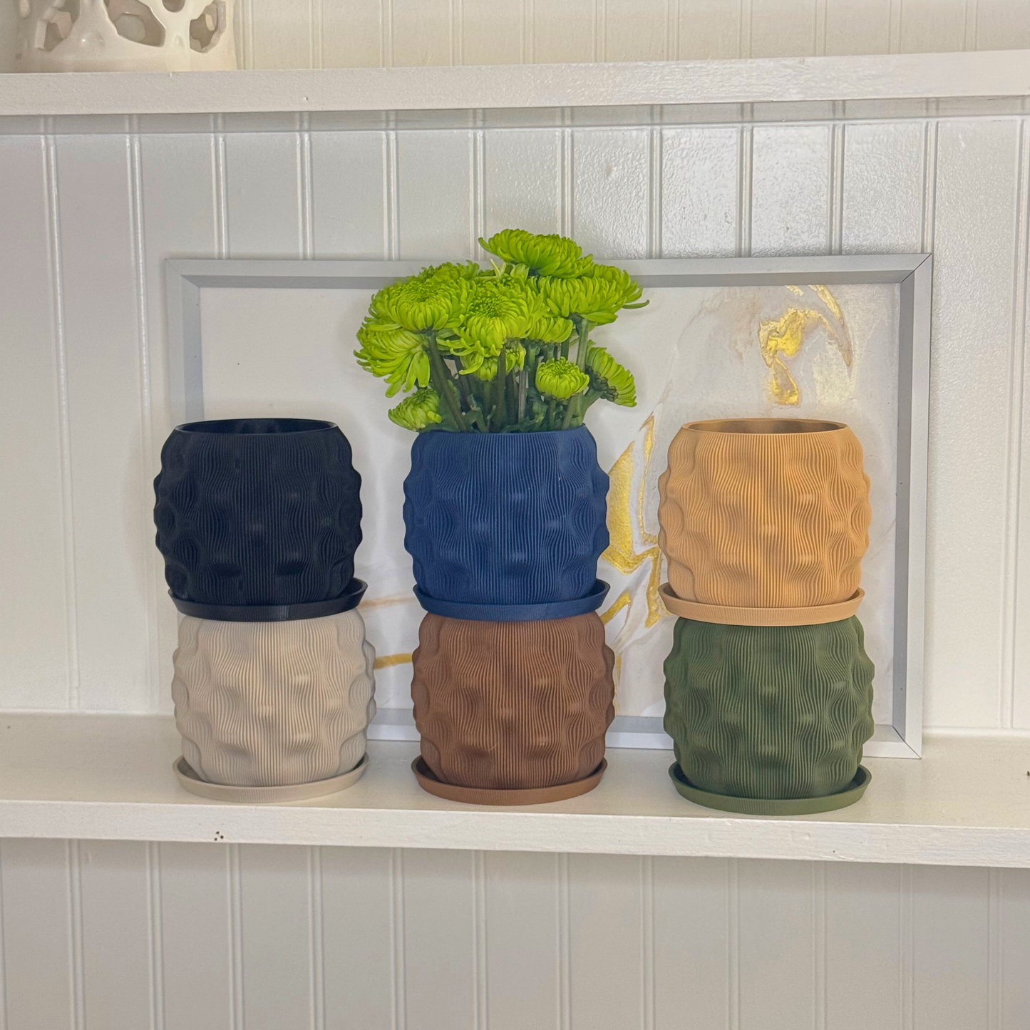 Colorful dimpled planters arranged on a shelf, featuring vibrant green flowers, highlighting a modern decor style.