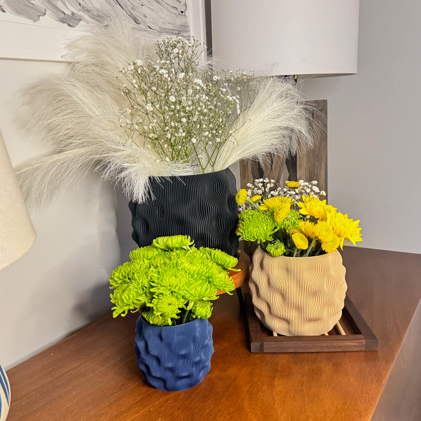 Stylish dimpled planters in various matte colors with vibrant flowers and decorative accents on a wooden surface.