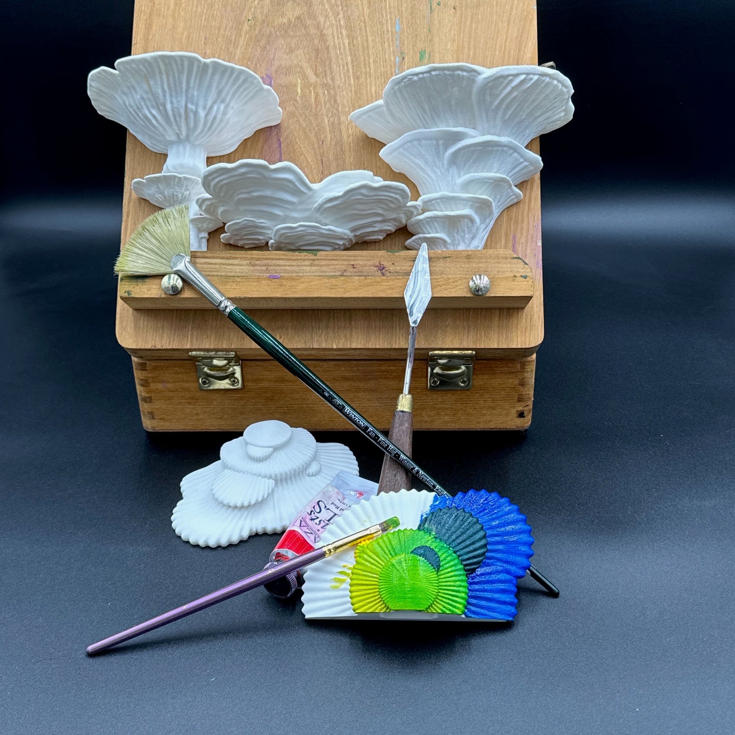 Creative arrangement of fungus-inspired white shelving units and painting tools on a dark surface, suitable for artistic decor.