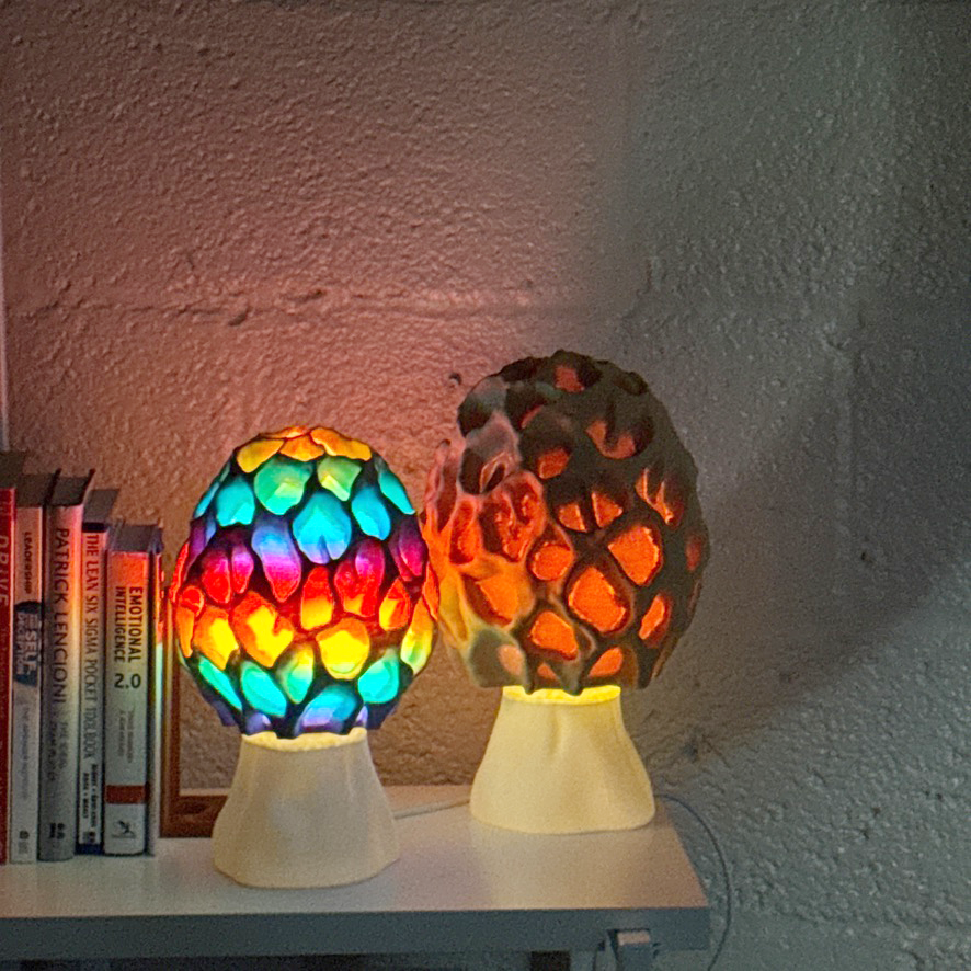 Two vibrant, illuminated Morel-style lamps with colorful designs on a table surrounded by books.