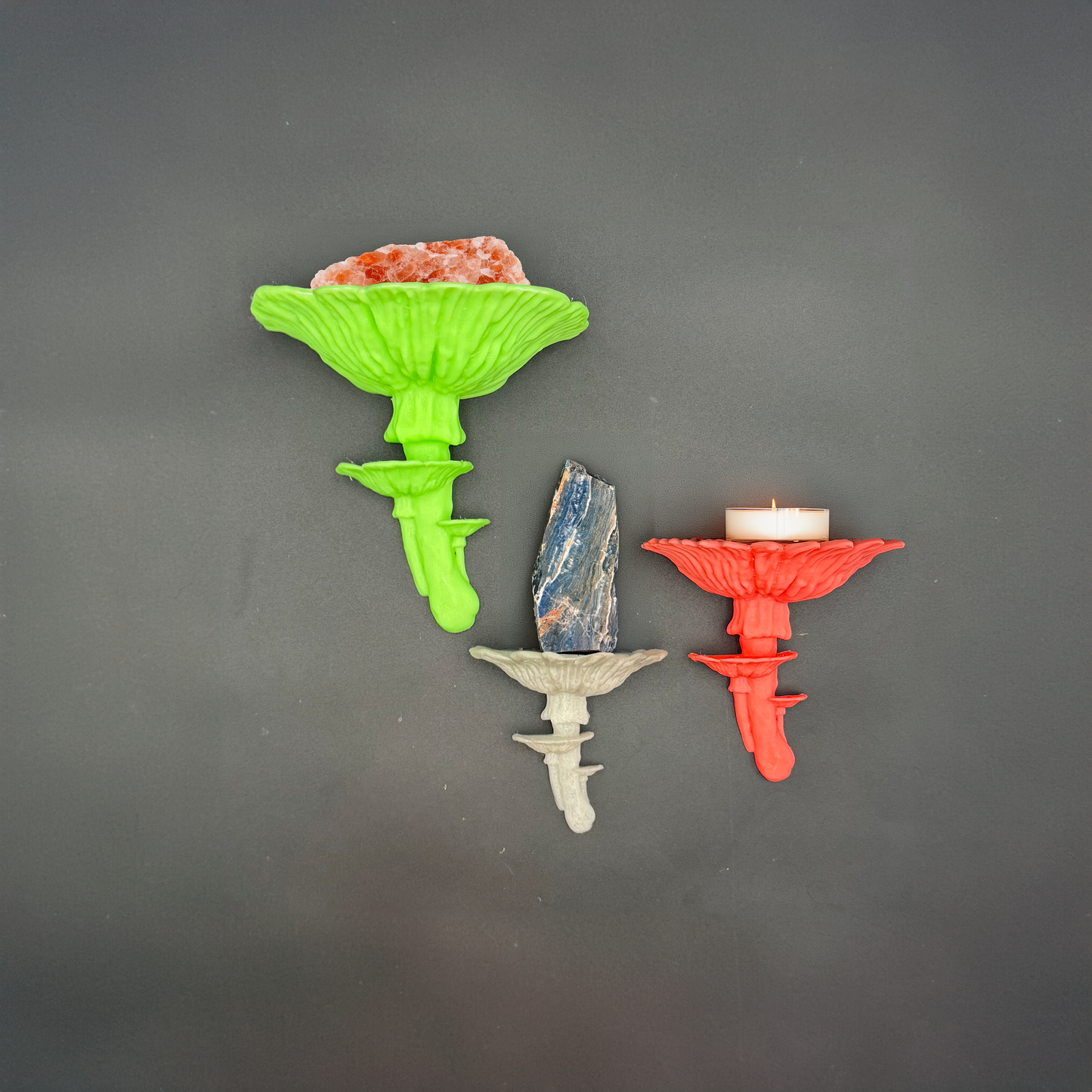 Three styled Amanita mushroom floating shelves in vibrant green, grey, and red, displaying unique decorative items like stones and a candle.