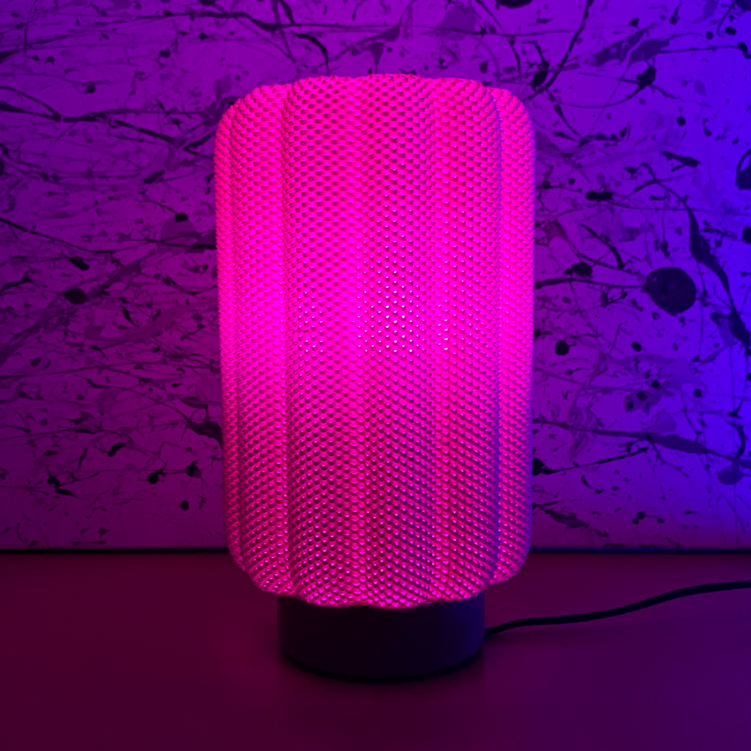 CARLA Table Lamp glowing in vibrant pink light, set against a colorful abstract background, adding a contemporary flair to interior design.