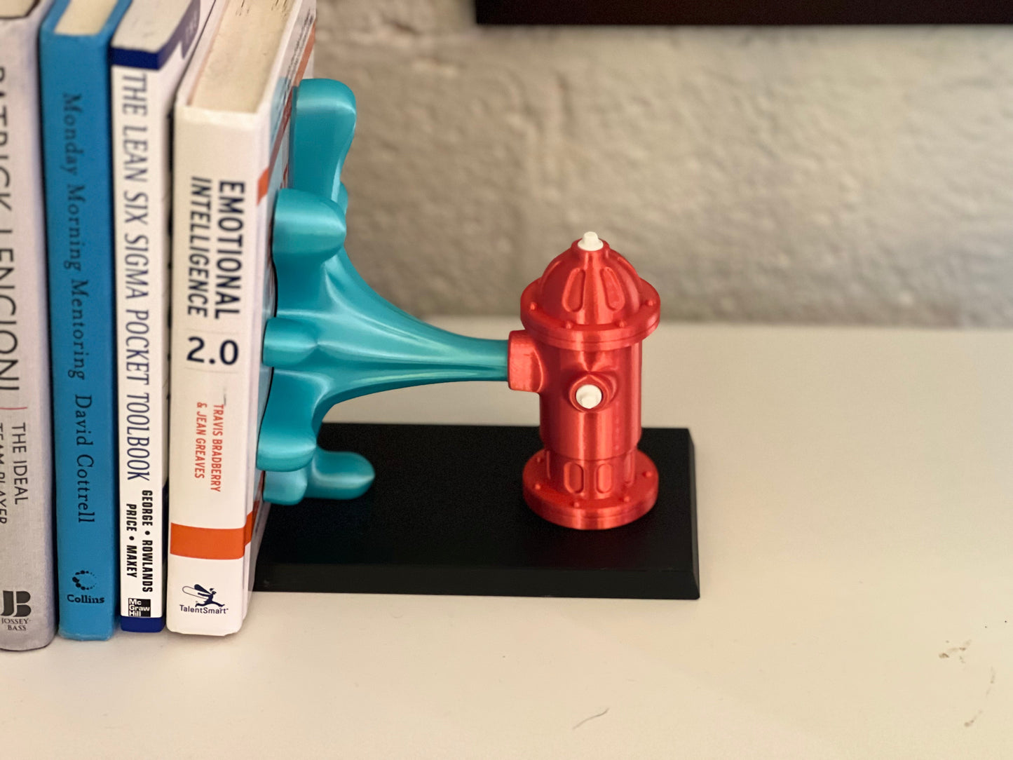 Colorful whimsical fire hydrant book end in vibrant red and turquoise, showcasing an imaginative design while supporting books on a white shelf.
