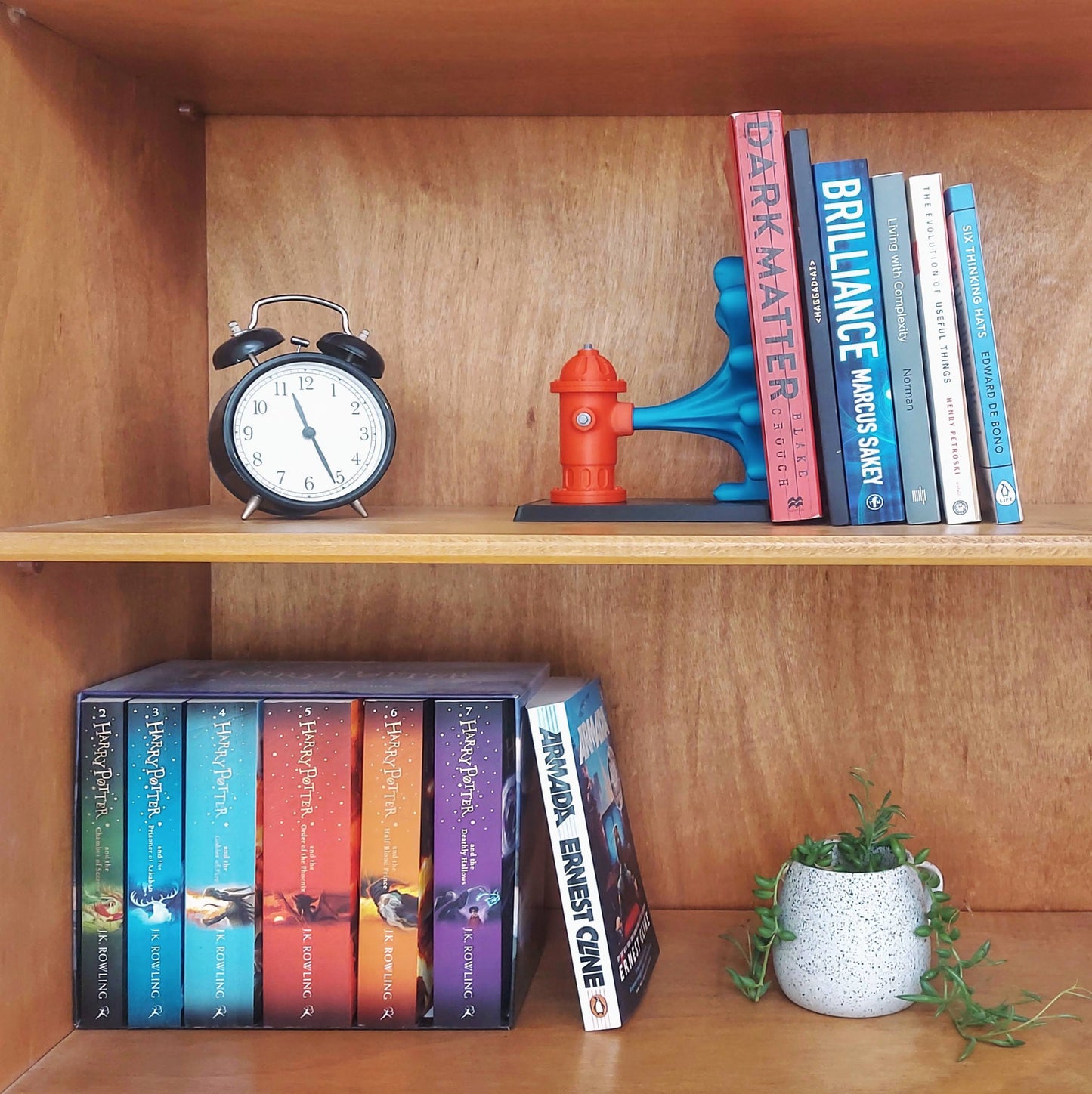 Charming wooden bookshelf displaying a colorful fire hydrant book end, featuring a vibrant red hydrant and blue water flow design with assorted books and a clock.