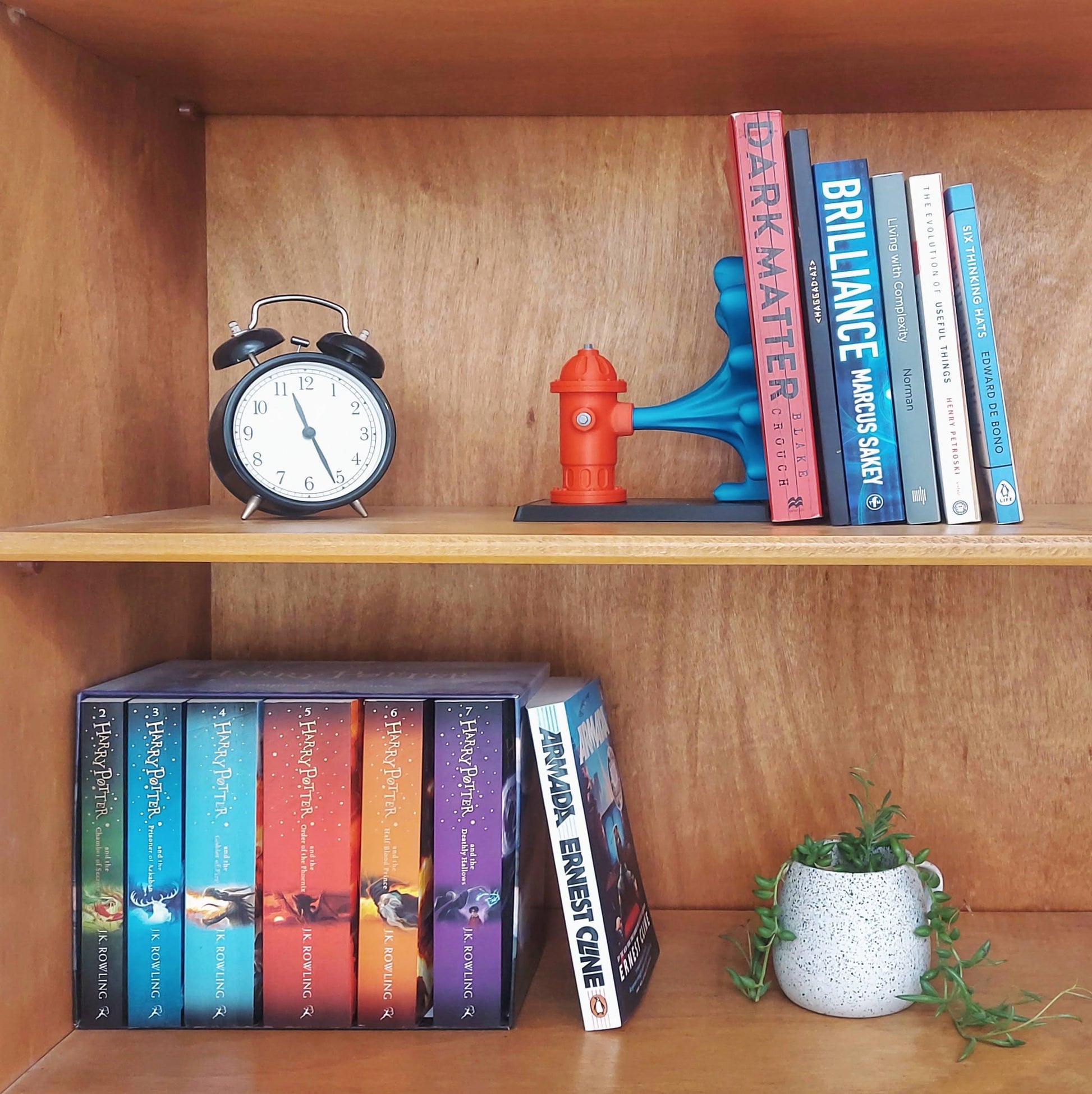Charming wooden bookshelf displaying a colorful fire hydrant book end, featuring a vibrant red hydrant and blue water flow design with assorted books and a clock.