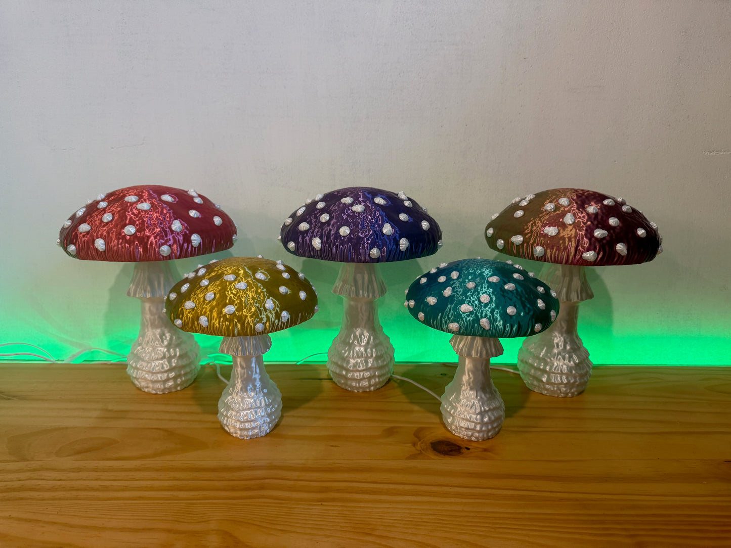 A colorful arrangement of five glowing Amanita fungi lamps in red, yellow, purple, blue, and green, enhancing a whimsical atmosphere in a cozy setting.