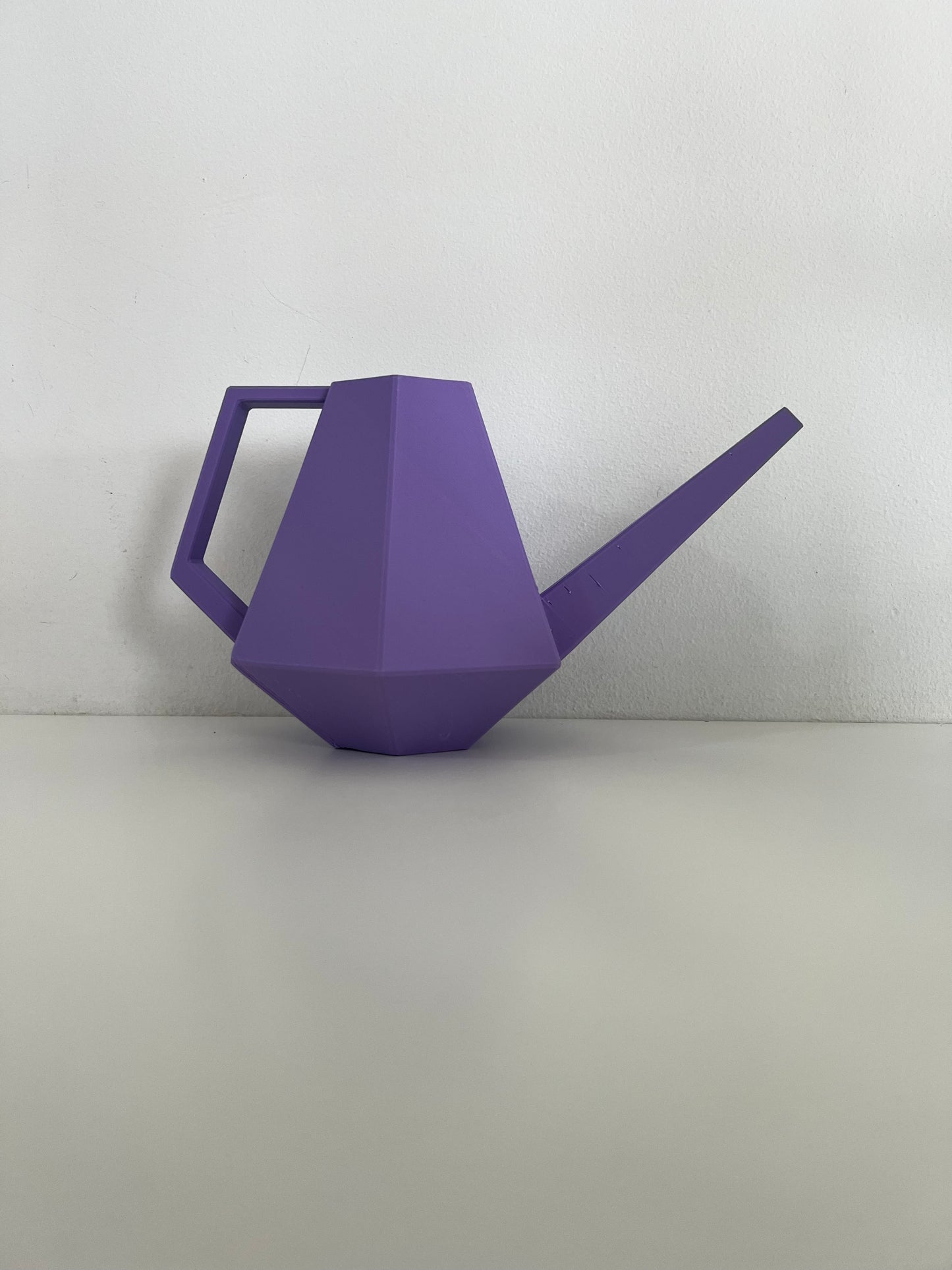 A close-up view of a purple geometric watering can on a white surface, highlighting its unique shape and design.