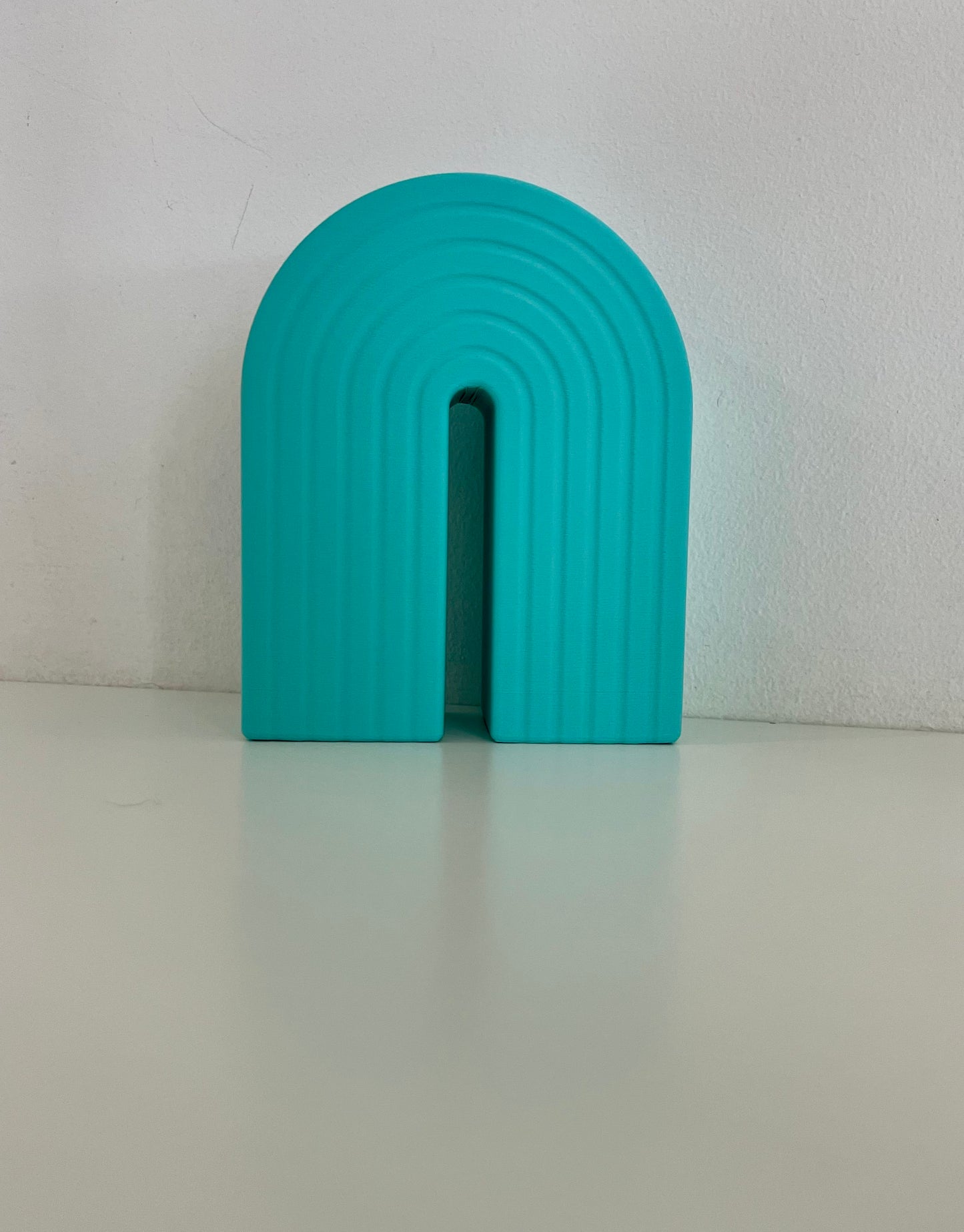 Single turquoise rainbow bookend, featuring a curved design with ribbed texture, great for supporting books or decorative items.