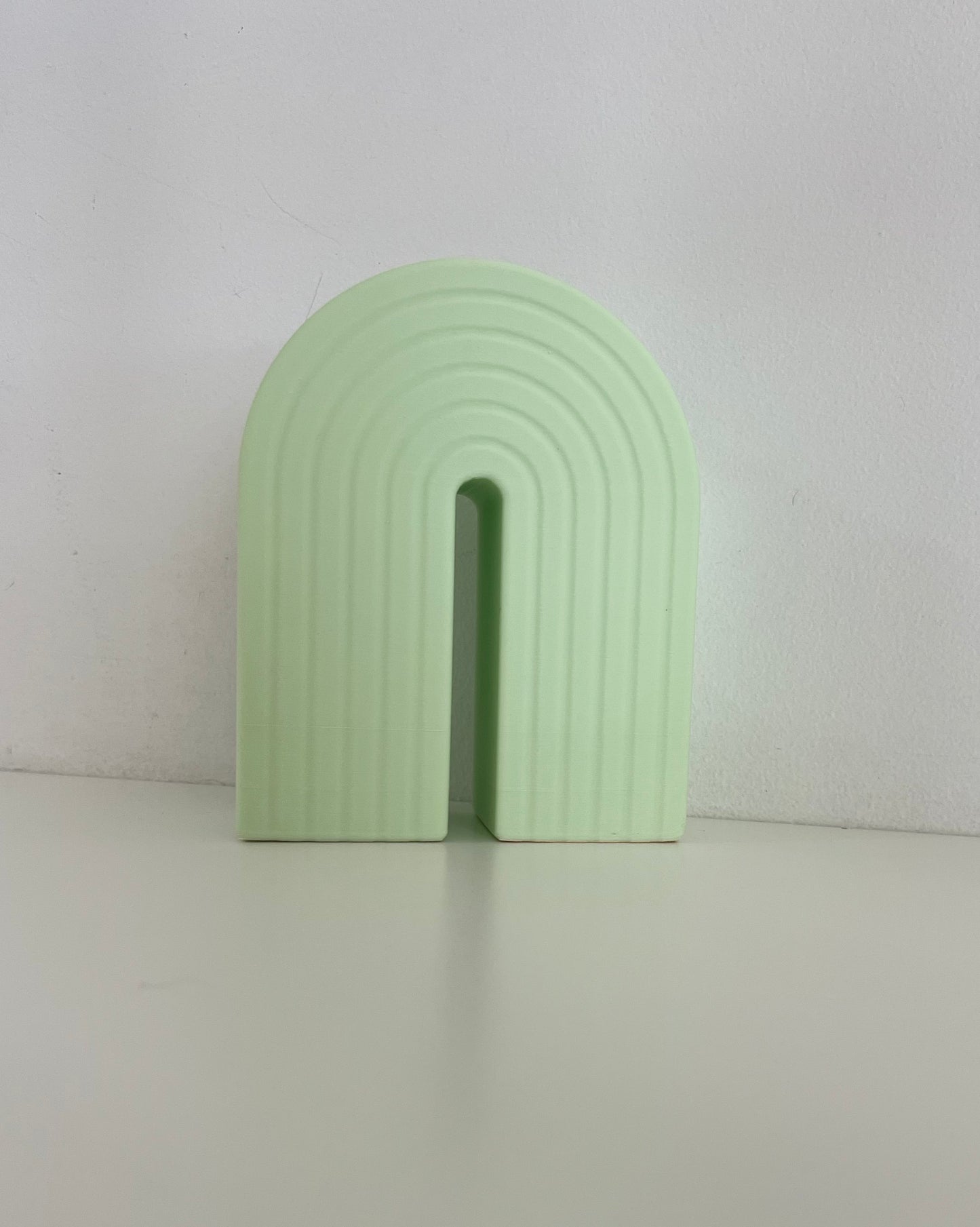 Sleek pastel green rainbow bookend, showcasing a stylish design with a ribbed finish, perfect for organizing books or displaying plants.