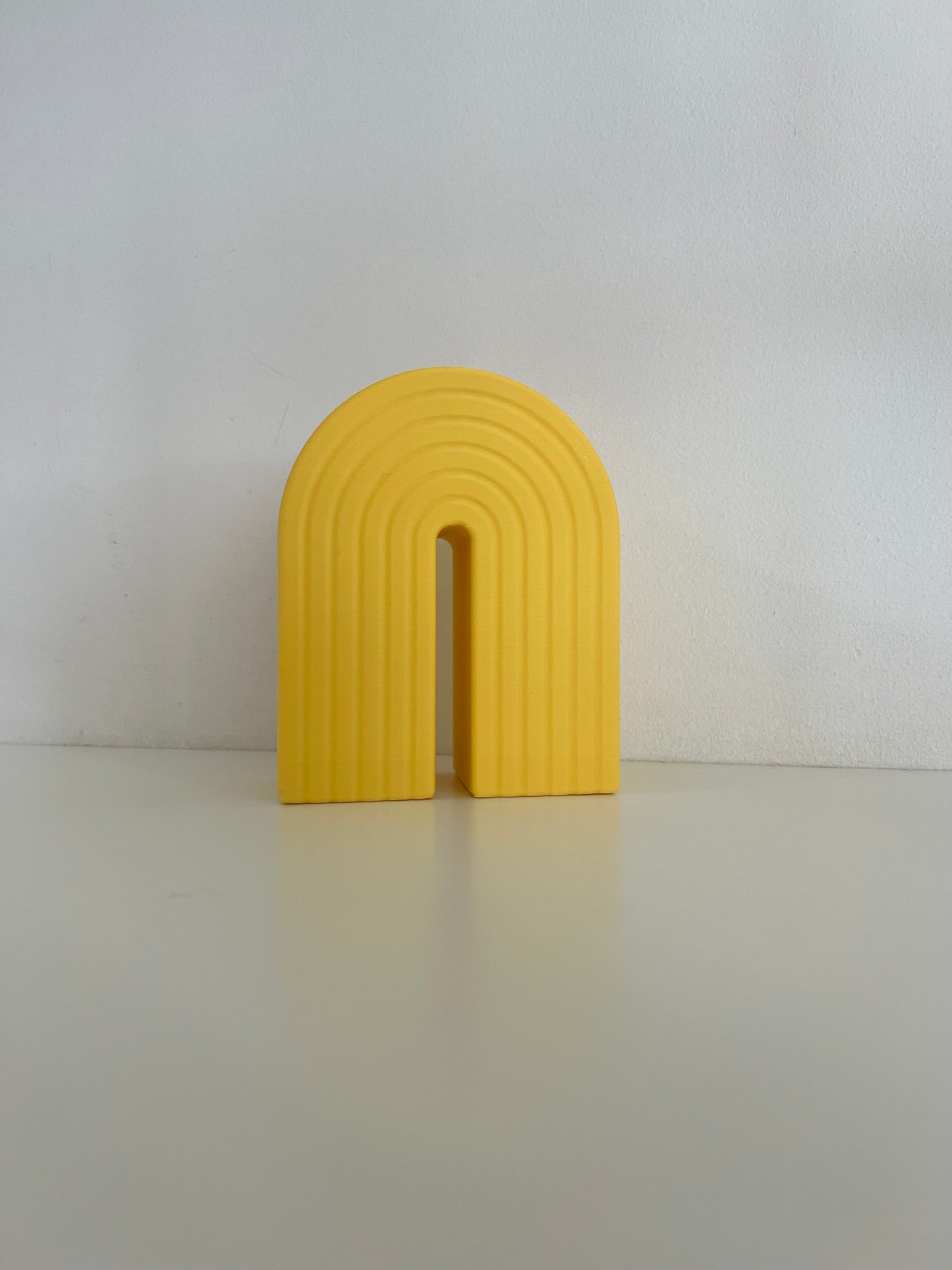 Bright yellow rainbow bookend with a ribbed texture, perfect for keeping books upright and adding a splash of color to any shelf.