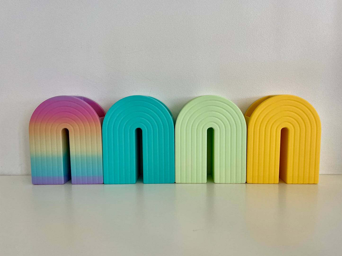 Vibrant rainbow-shaped bookends in shades of turquoise, green, yellow, and purple, ideal for adding a fun touch to office or home decor.