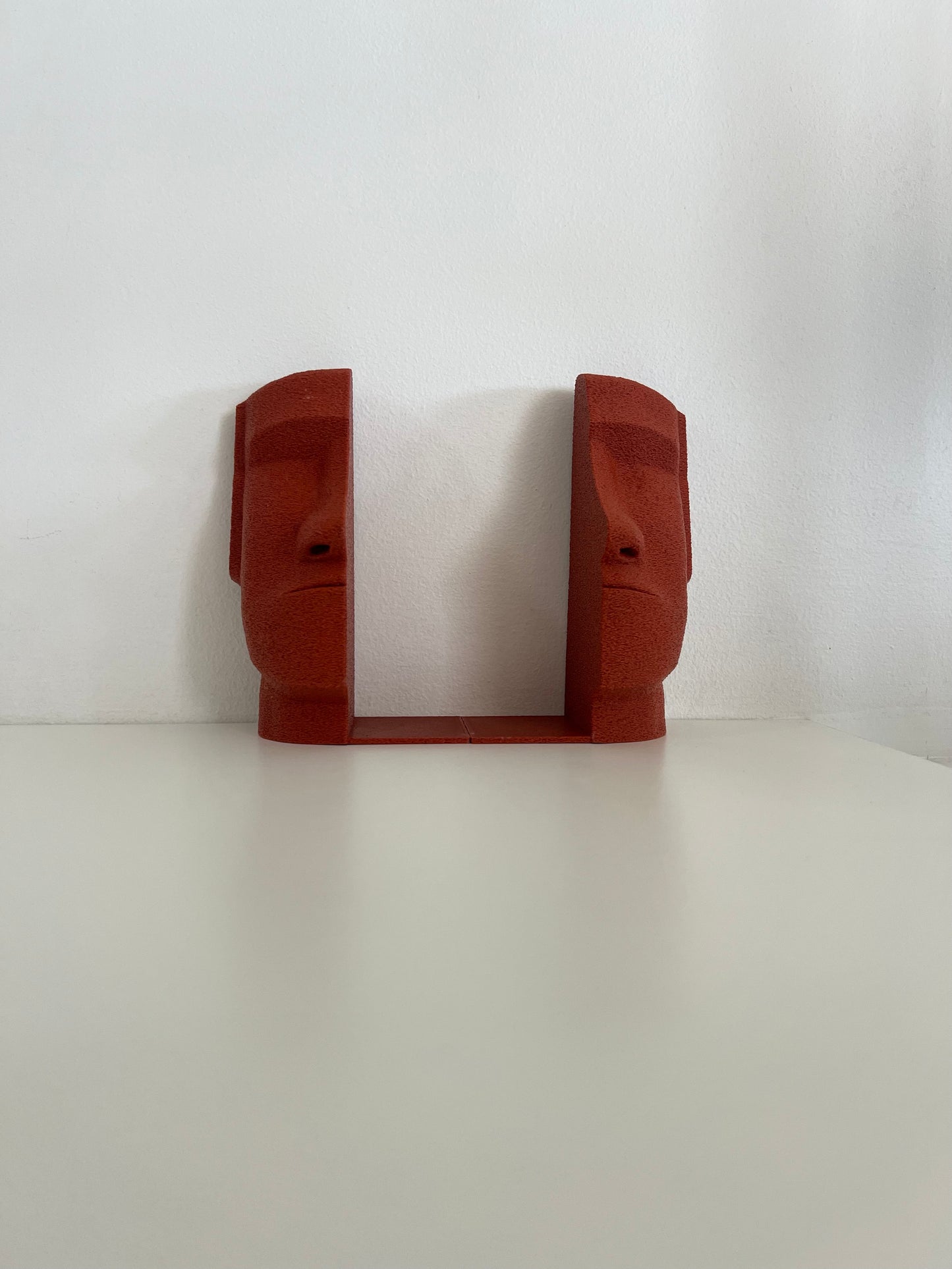 Stylish red Moai bookends positioned symmetrically on a shelf, adding a pop of color to the decor.