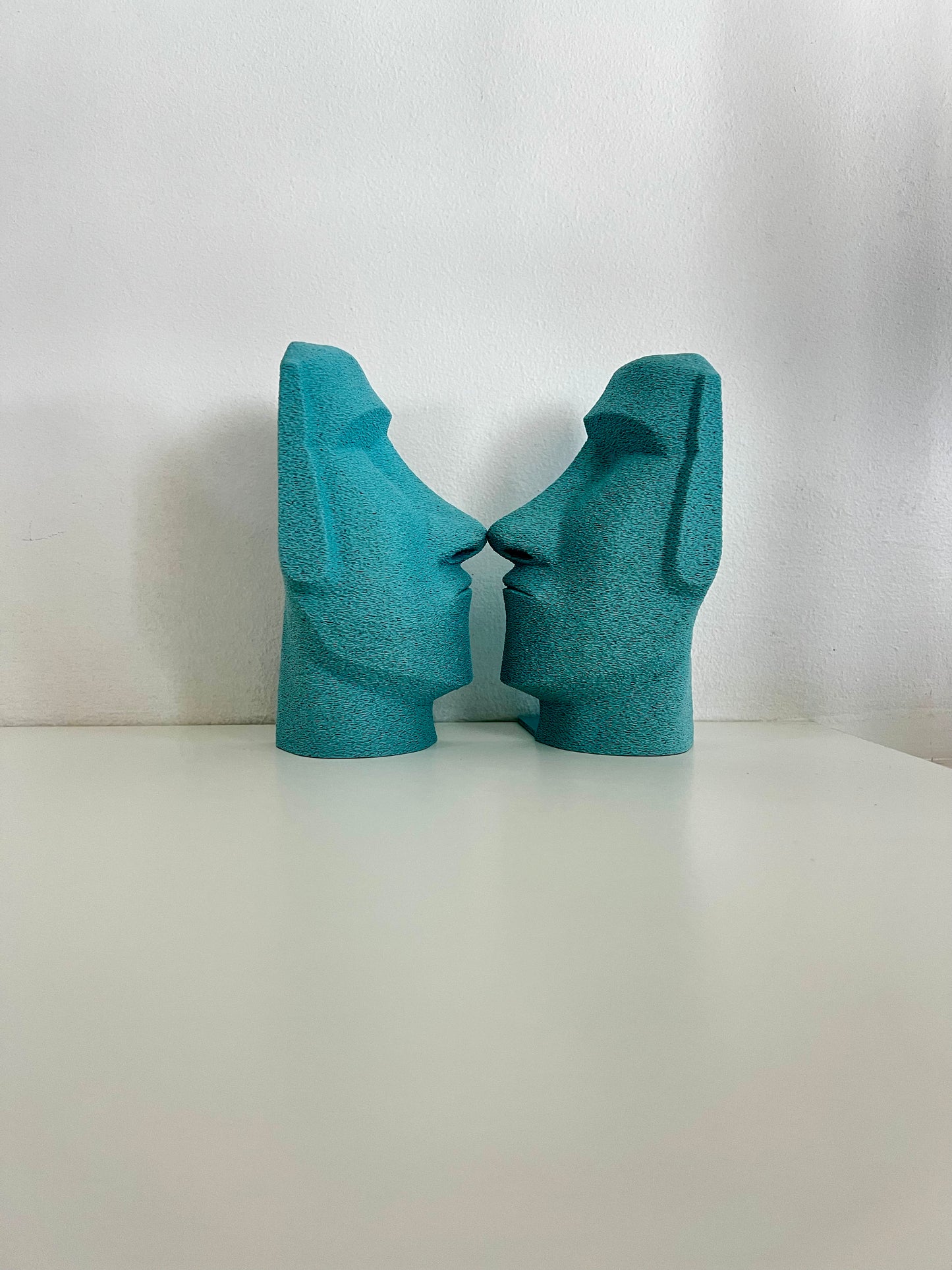 Turquoise Moai bookends centered between books, providing an artistic support for reading materials.