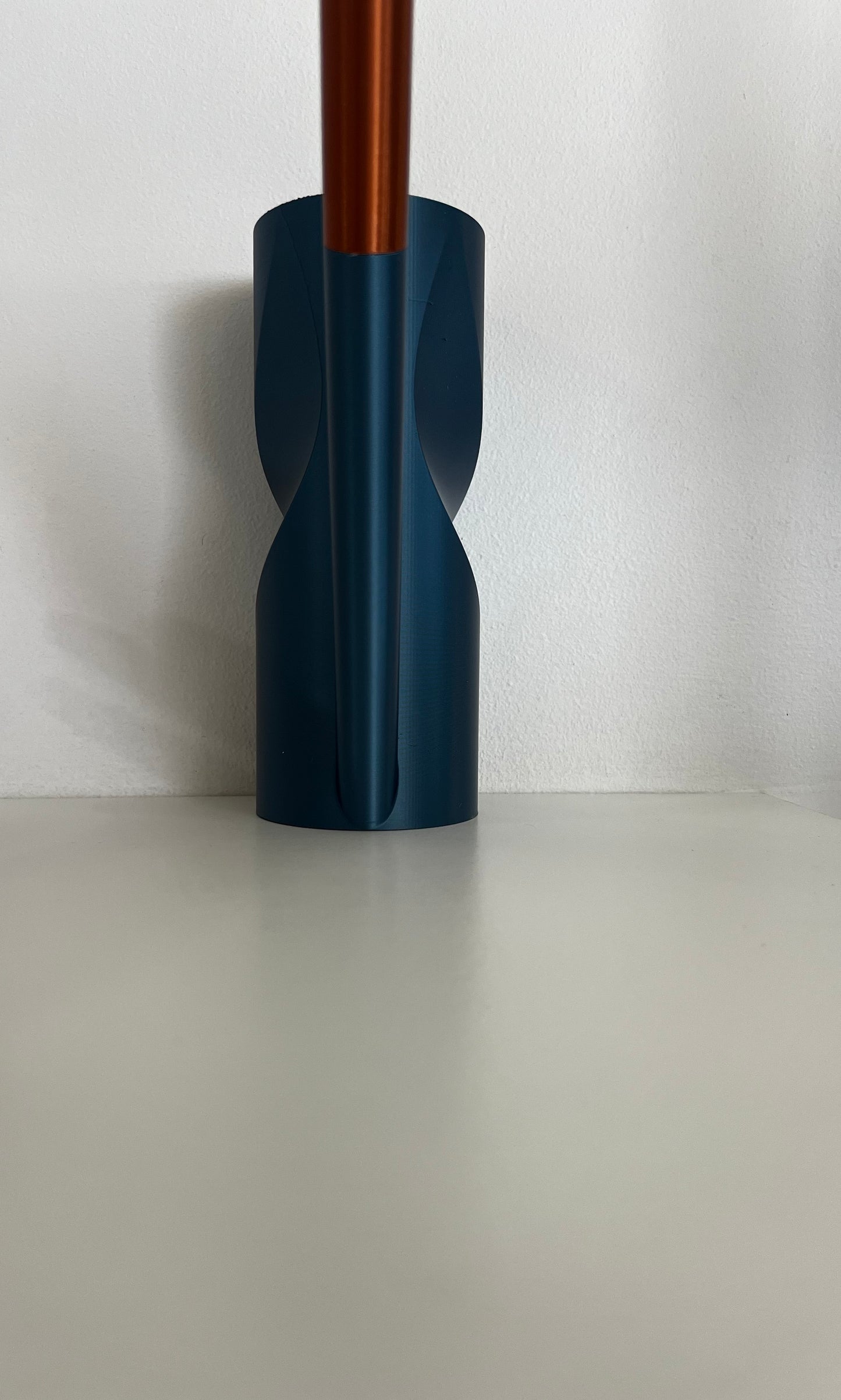 A modern teal watering can with a copper spout, beautifully arranged on a simple white table.