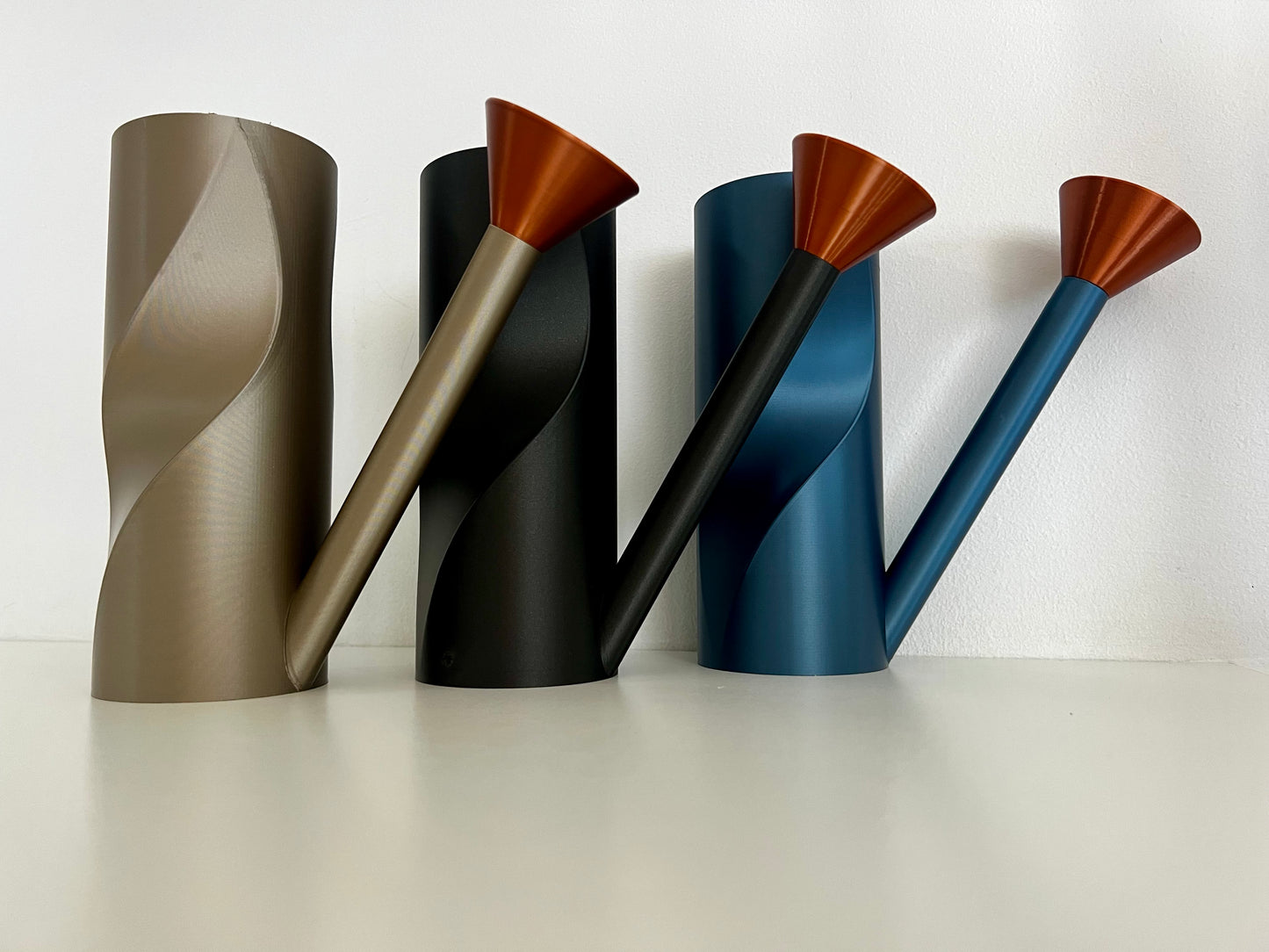 Three contemporary watering cans in bronze, black, and blue, showcasing their sleek design and copper spouts.