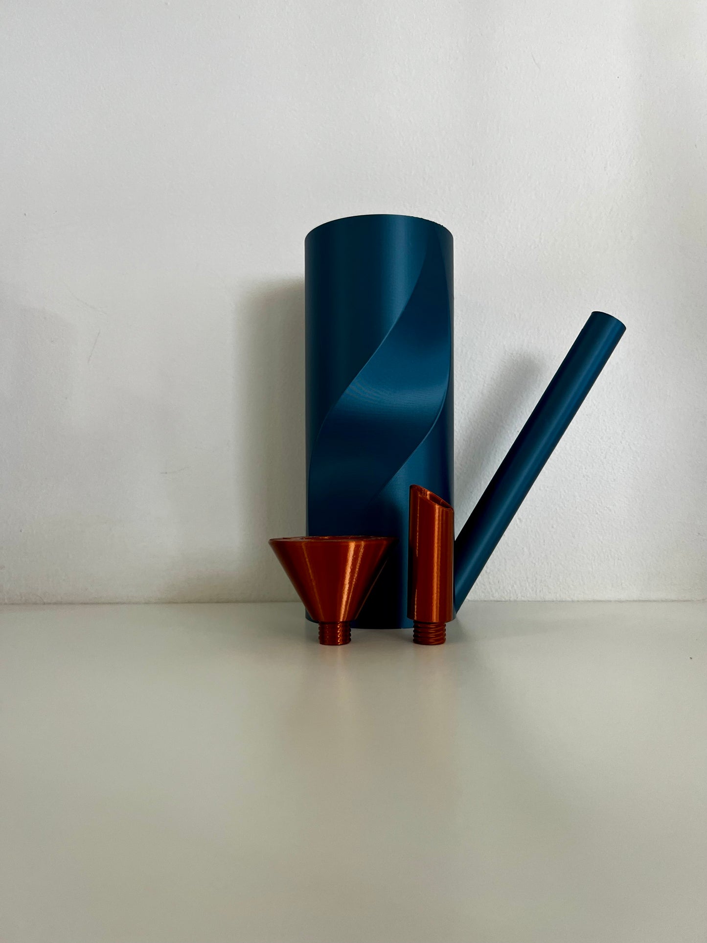 A minimalist blue watering can next to two detachable spouts, one straight and one flared, on a white surface.