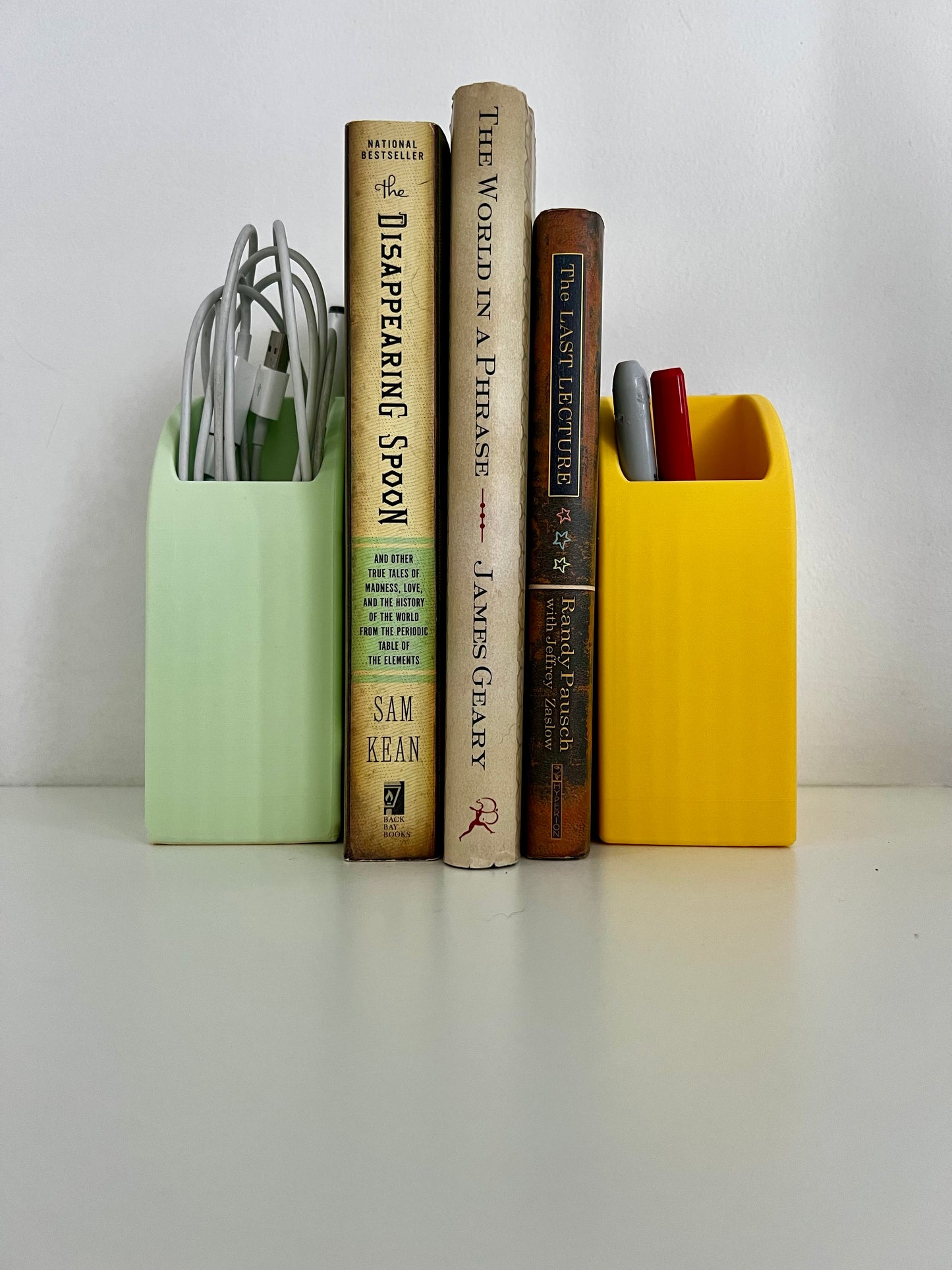 Colorful bookend organizer holding books and pens on a stylish desk, featuring pastel green and yellow containers, perfect for a tidy workspace.