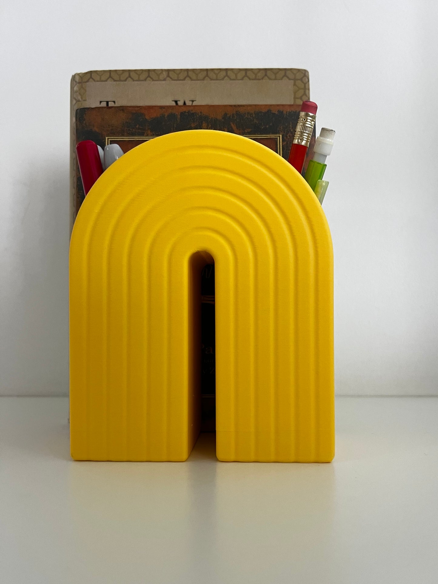 Colorful bookend organizer featuring a bright yellow rainbow design, surrounded by books and writing instruments, enhancing workspace flair.