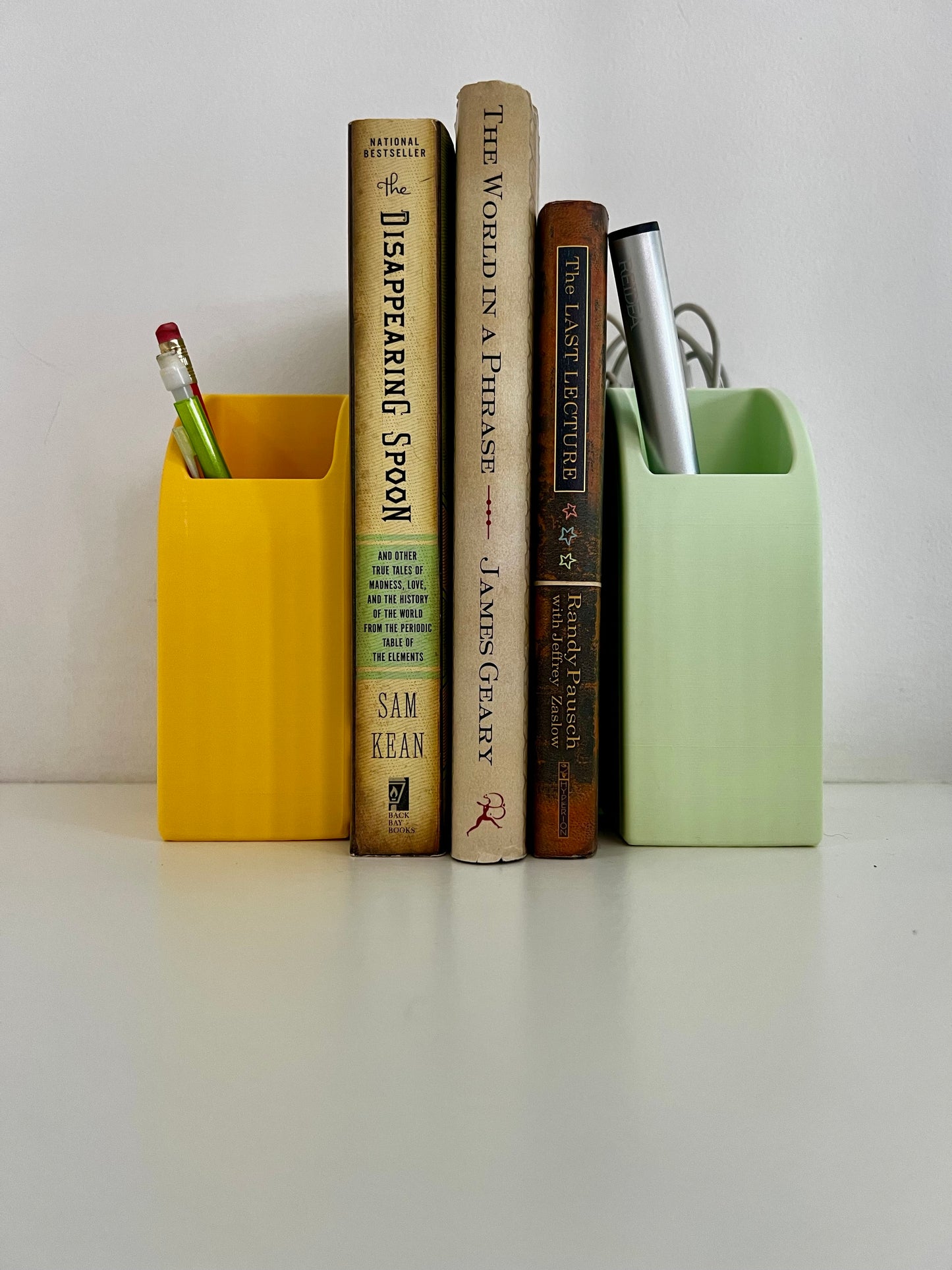 Minimalist desk scene with yellow and green rainbow bookends, organizing books alongside colorful pens for an artistic touch.