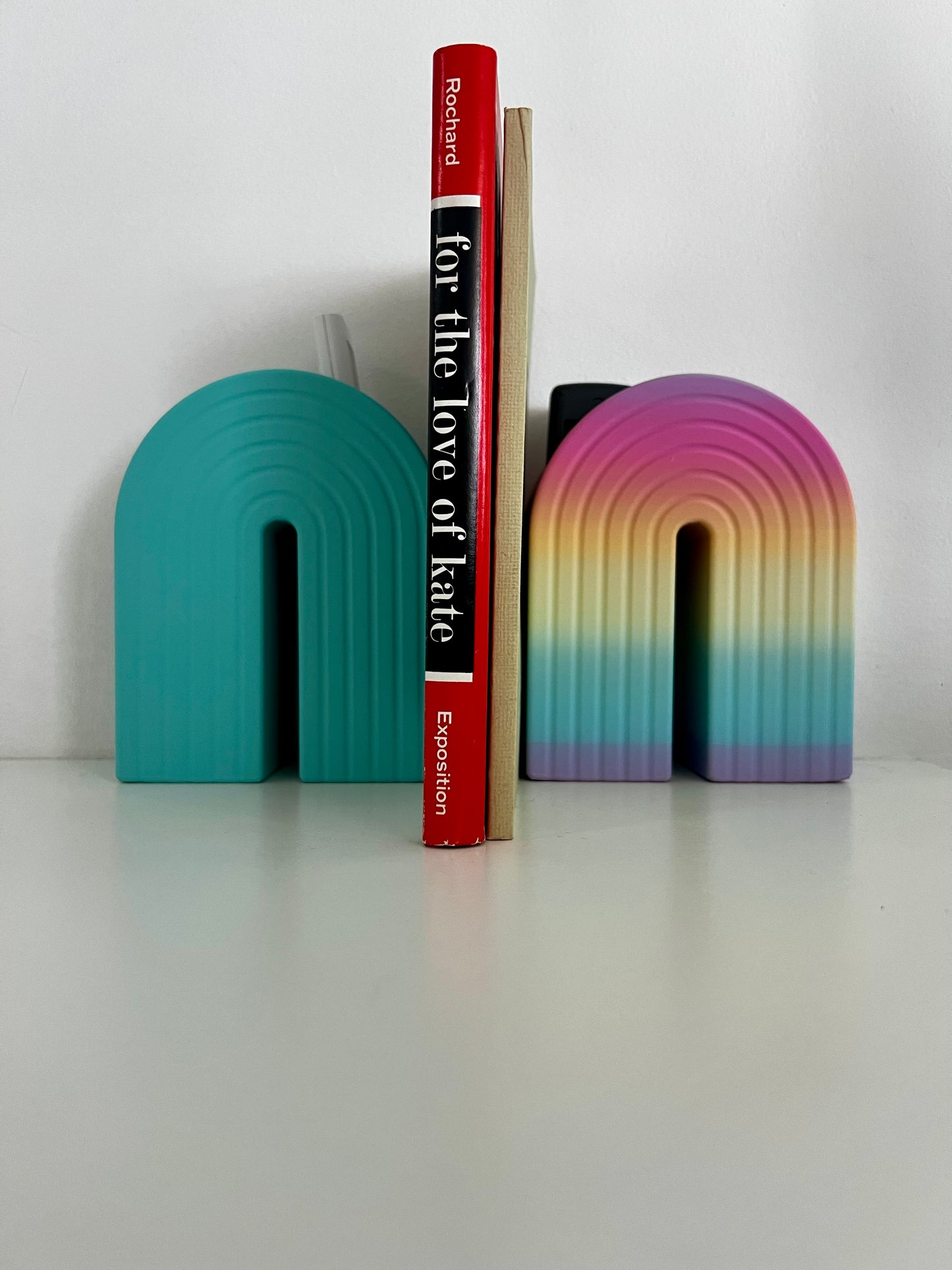 Fresh turquoise rainbow bookend with a bright design, stylishly supporting a book while showcasing a pen for a playful workspace.