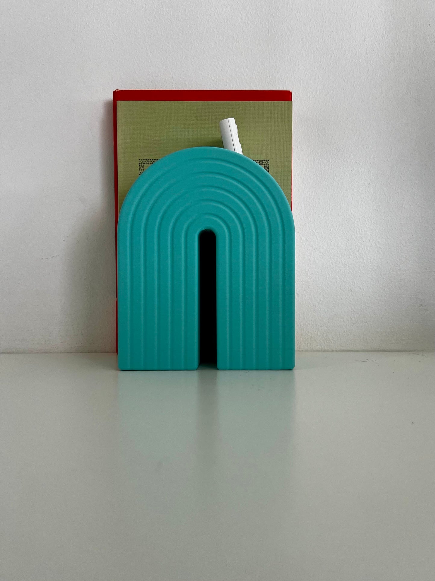 Cheerful desk featuring teal rainbow bookends with a book and pen nestled between them, ideal for a creative work environment.