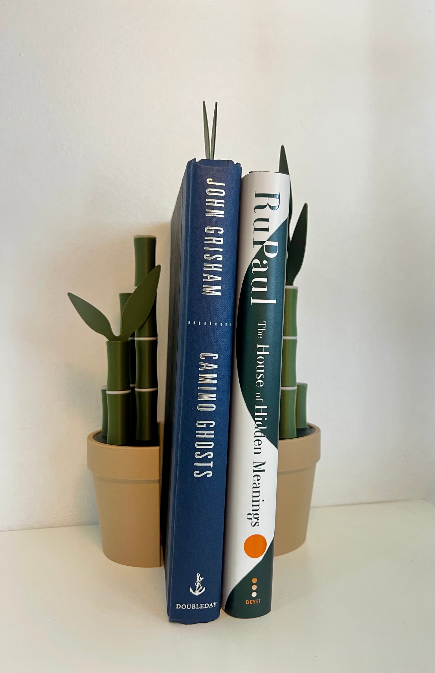 Bamboo bookend set with included bamboo leaf-shaped bookmarks, organized between two books by John Grisham and RuPaul.