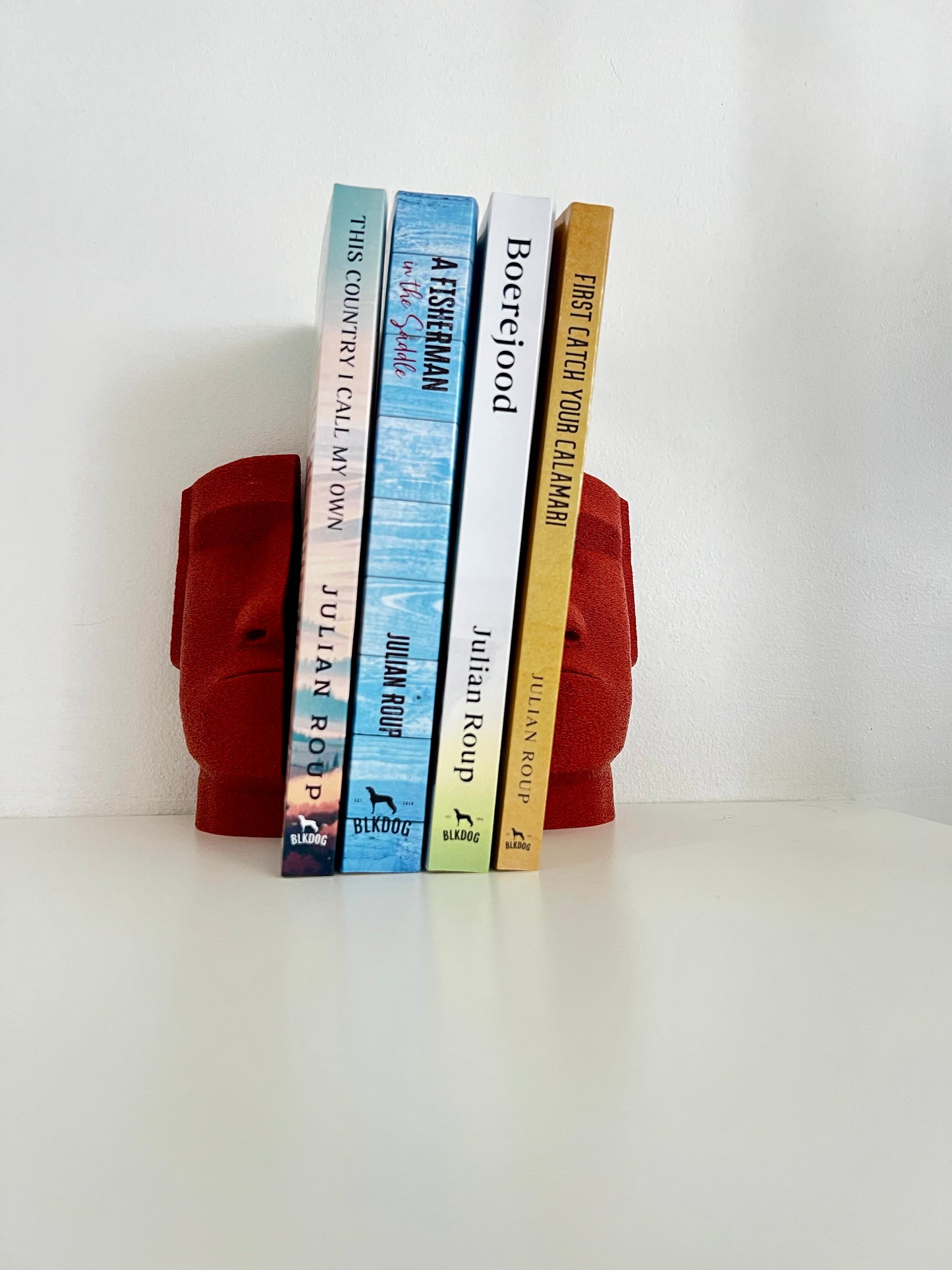 Red Moai bookends accentuating a stack of books, perfect for home or office bookshelf decor.
