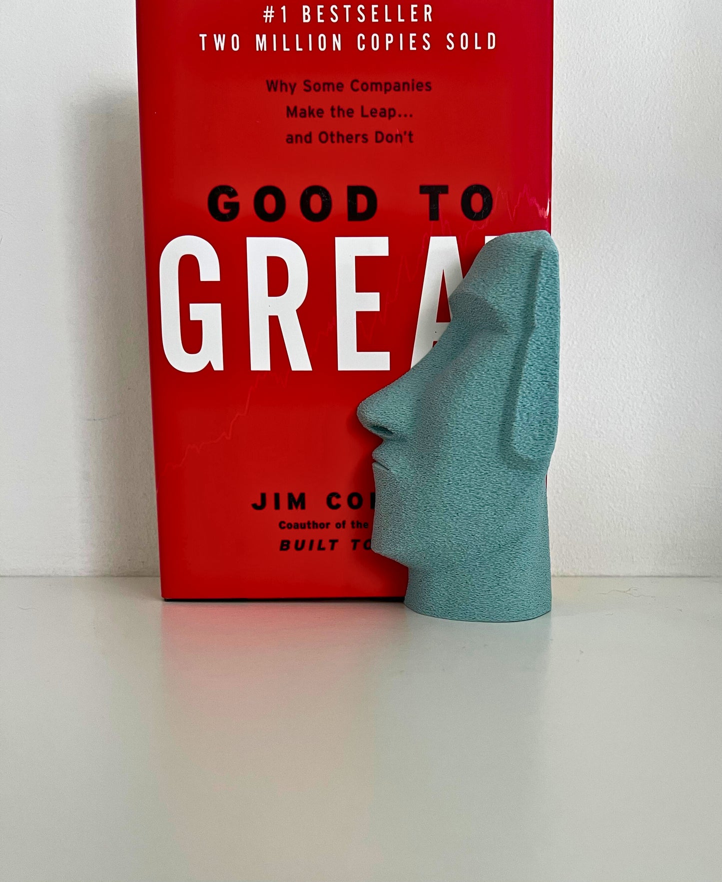 Profile view of a turquoise Moai bookend next to a bestselling business book, creating a stylish arrangement.