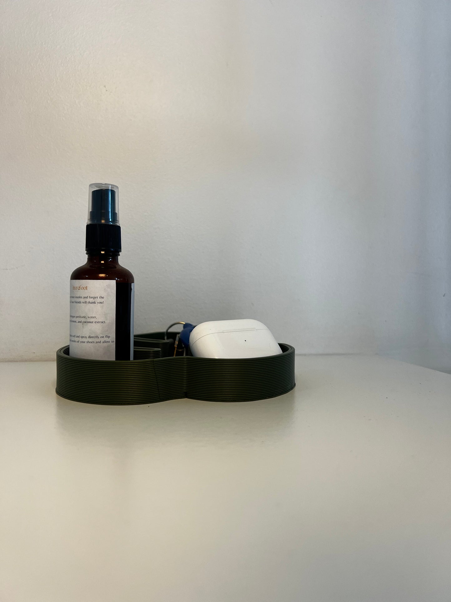 Minimalist green tray in Monstera leaf shape, holding a bottle and earbuds on a simple backdrop.