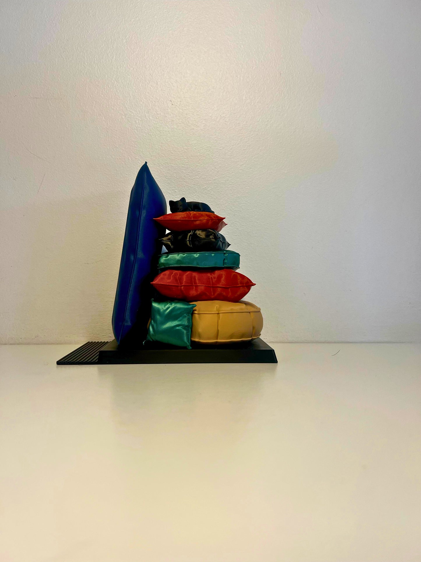 Side view of a playful bookend featuring a stack of colorful pillows with a curled-up cat on top, perfect for book lovers and cat enthusiasts.