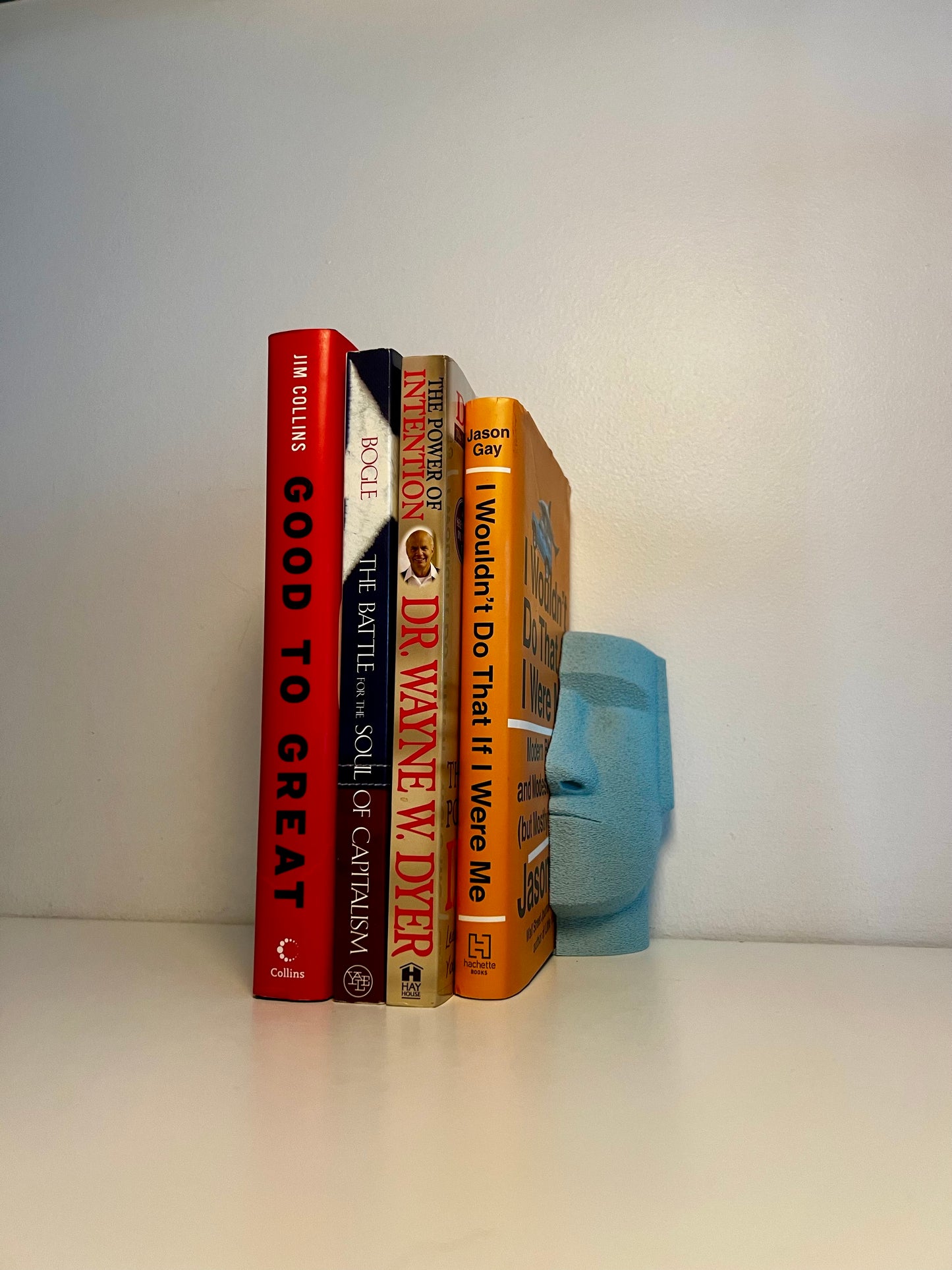 A blue Moai bookend nestled between colorful books, enhancing the visual appeal of a minimalist shelf.