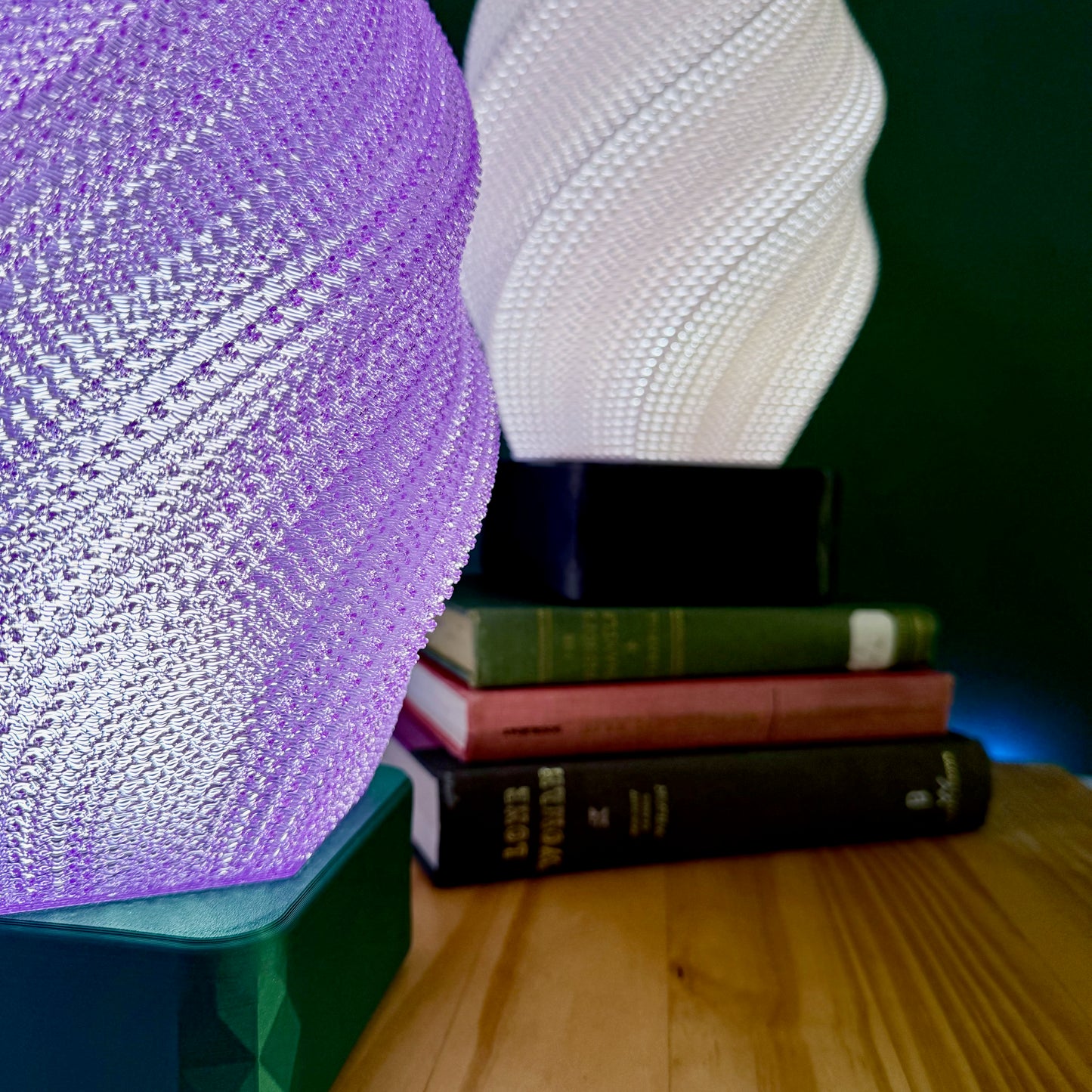 Close-up of a purple and a white spiral lamp glowing above a stack of hardcover books.