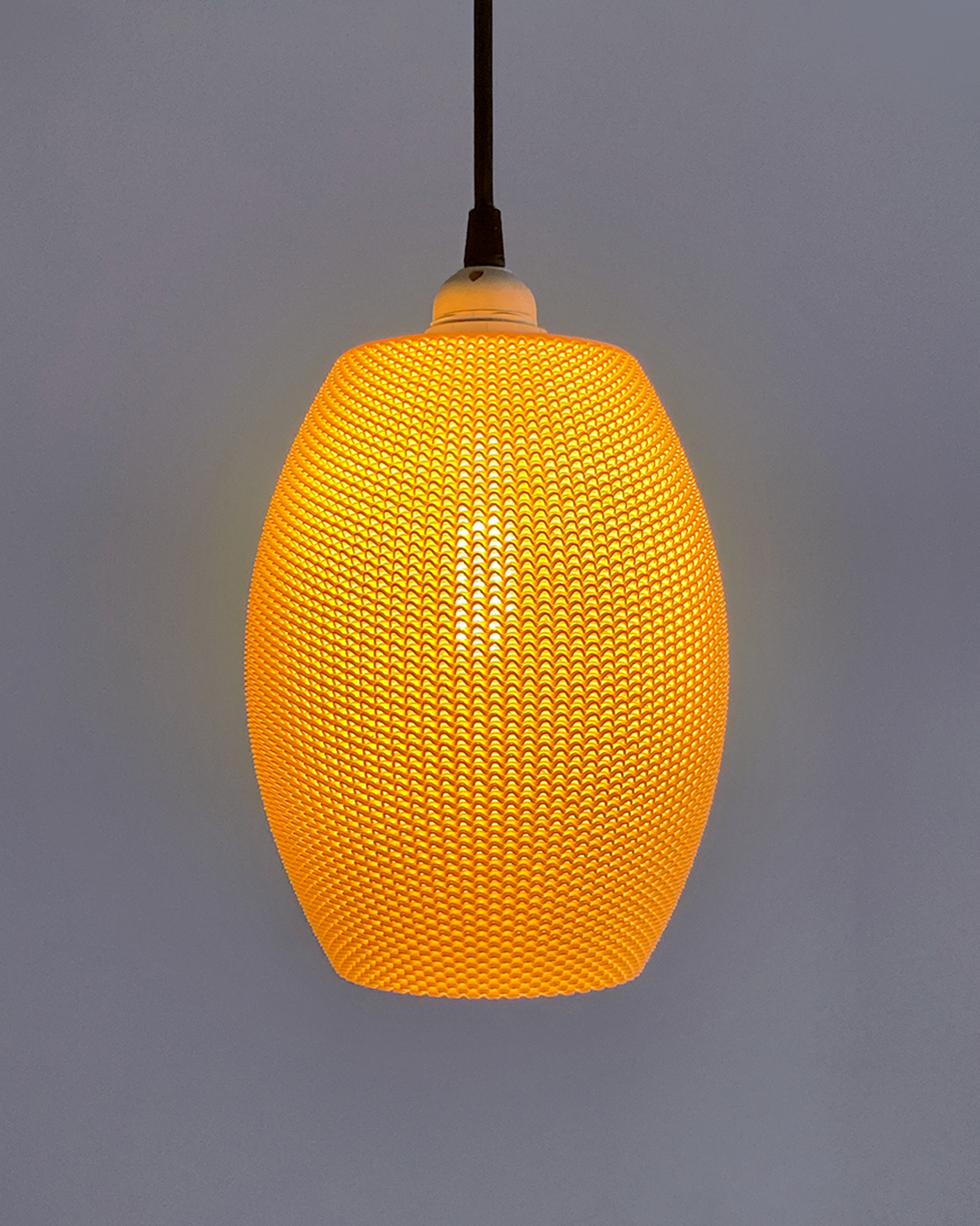 Ovo Lampshade in a warm orange hue, showcasing its elegant oval design, illuminated, offering a cozy atmosphere for modern home décor.