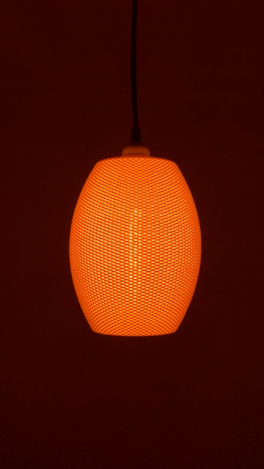 Ovo Lampshade in a vibrant orange, radiating warmth in a dimly lit environment, creating a welcoming ambiance.