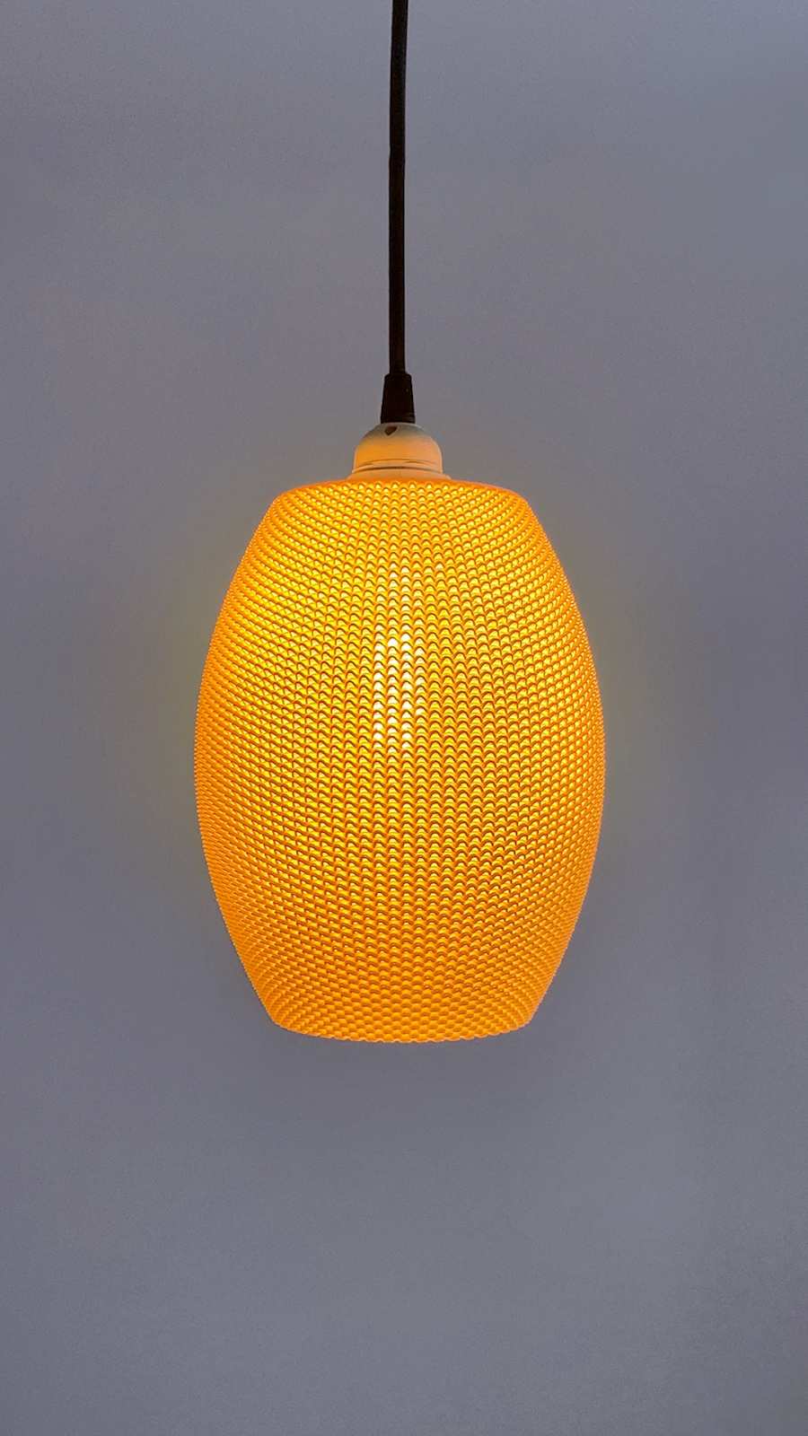 Ovo Lampshade illuminated in a vibrant orange against a gray background, showcasing its contemporary design.