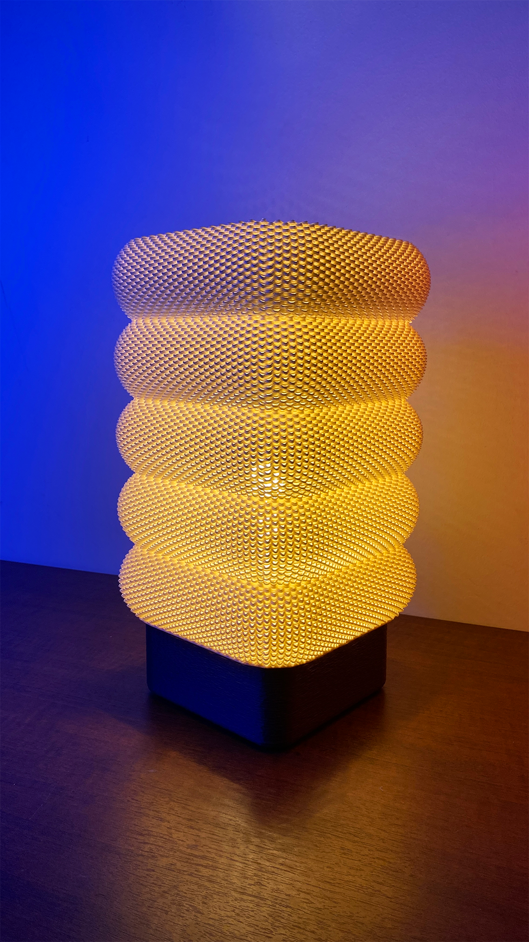 Another angle of the SARA Table Lamp displaying its modern design, emitting a warm light and complimenting the blue background.