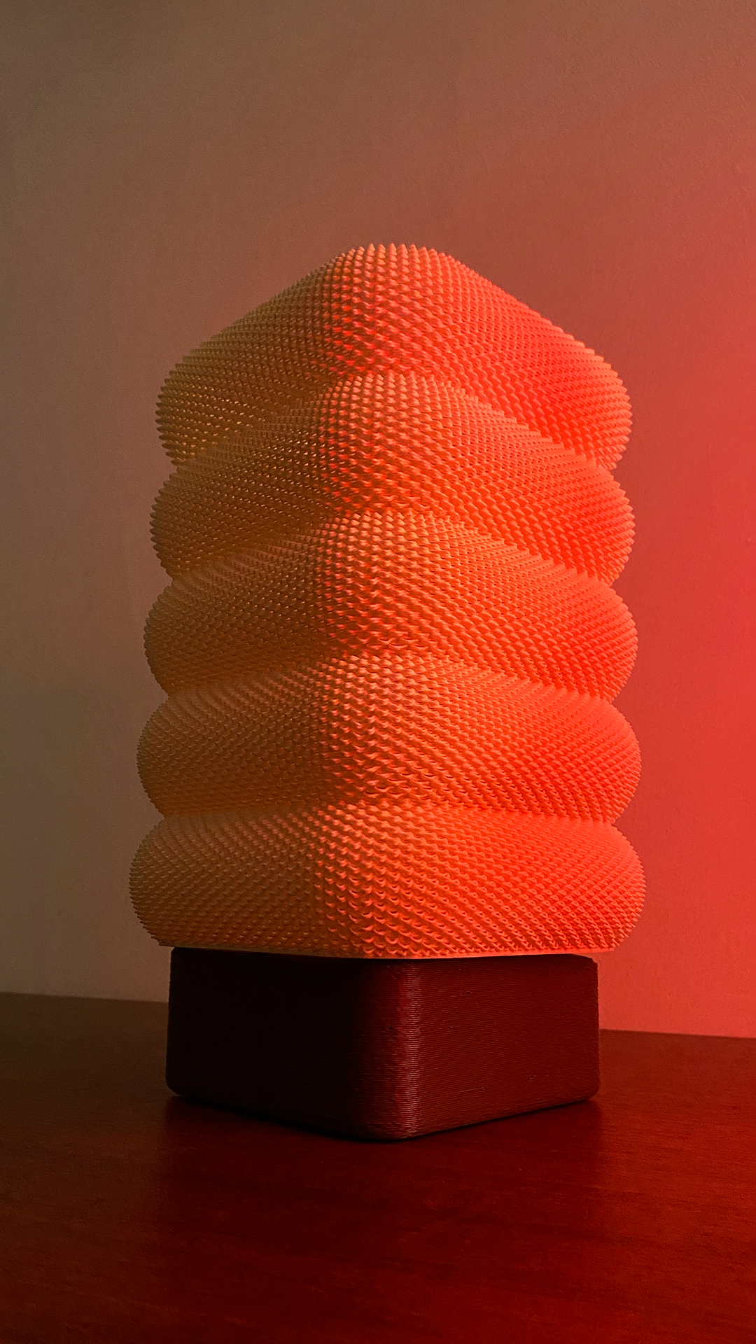 SARA Table Lamp featuring vibrant orange illumination, showcasing its stylish textured layers against a softly lit background.