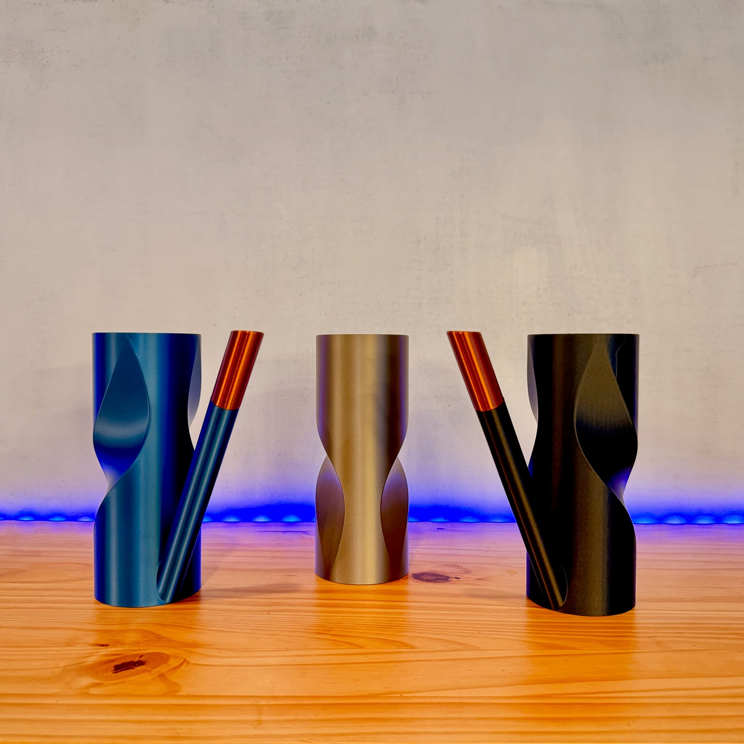 A trio of modern watering cans in blue, silver, and black with copper accents, set against a neutral backdrop.
