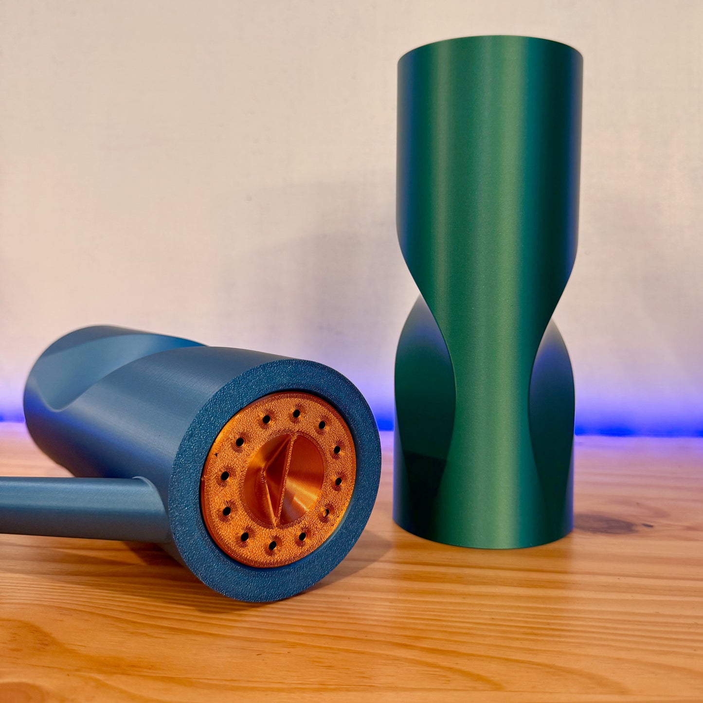 A stylish blue and green watering can featuring a removable copper spout, artfully arranged on a wooden surface.