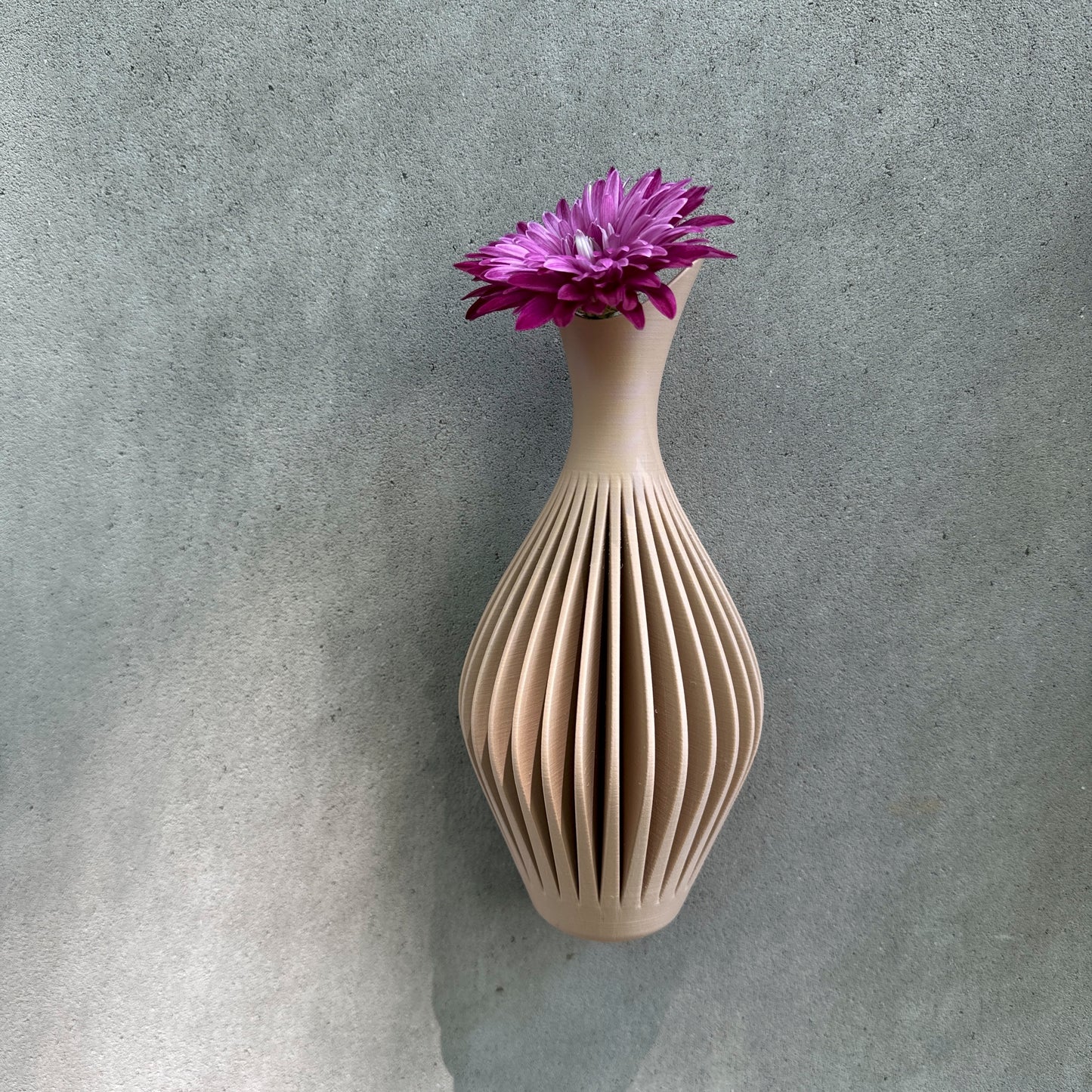 Close-up of a beige ribbed wall vase featuring a vibrant pink flower, set against a gray wall, showcasing its modern design.