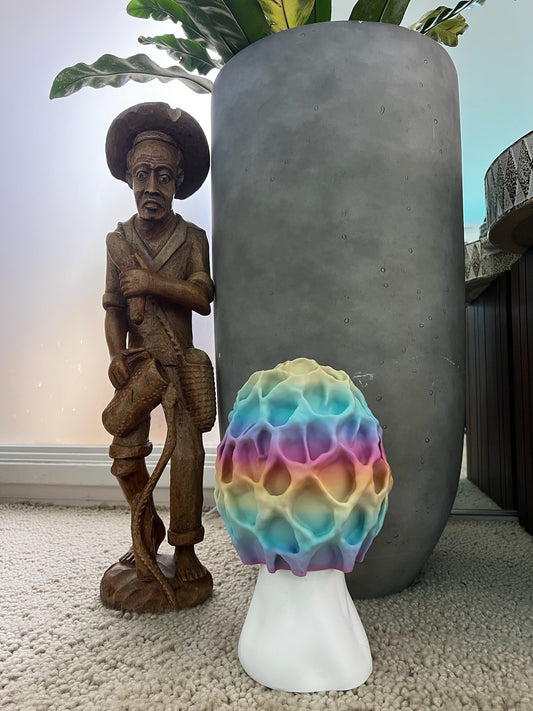 Colorful Morel-inspired illuminated table lamp next to a decorative wooden figure and potted plant.