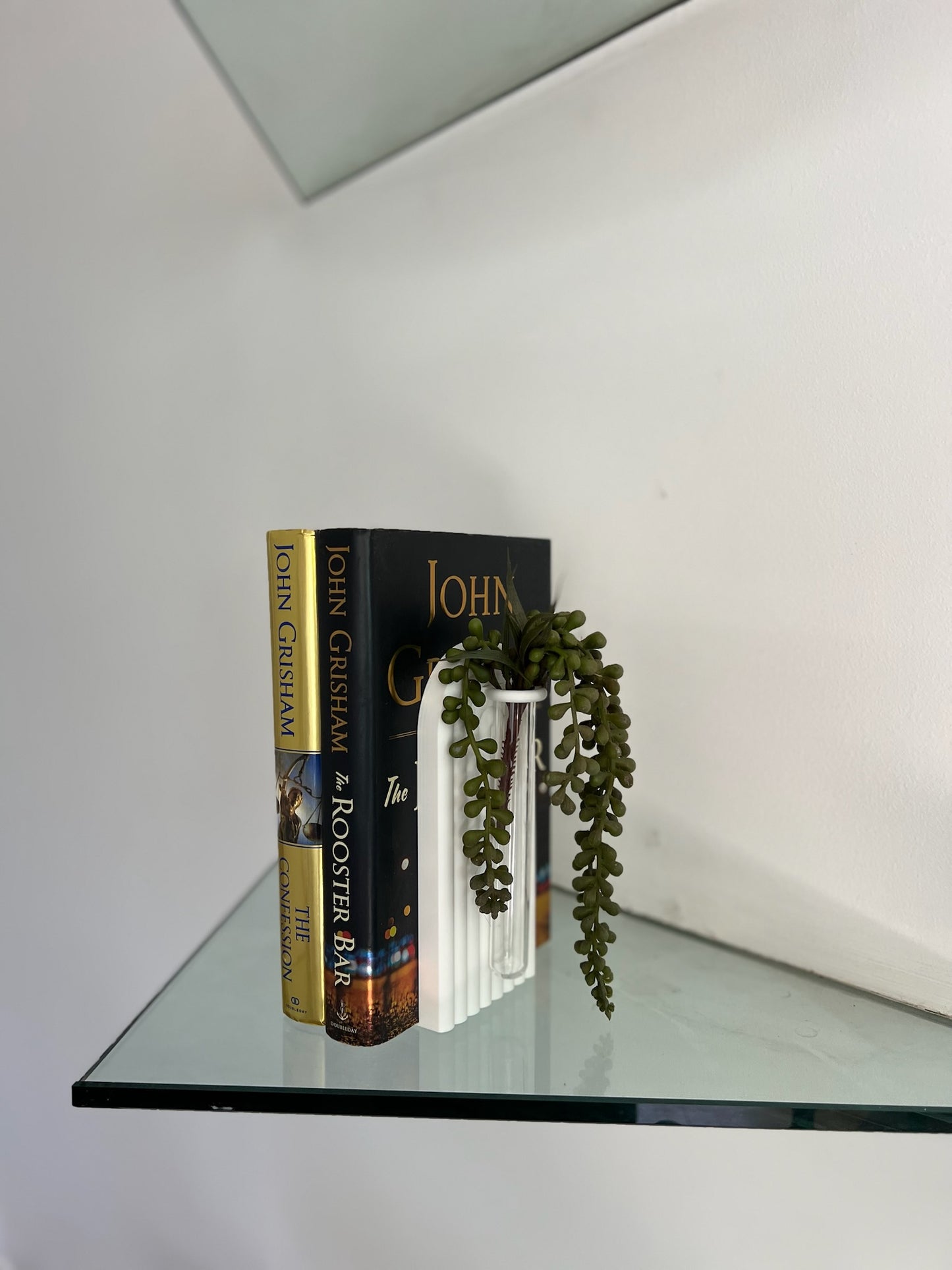 Stylish white propagation bookend featuring a green succulent, elegantly paired with dark books on a glass shelf.